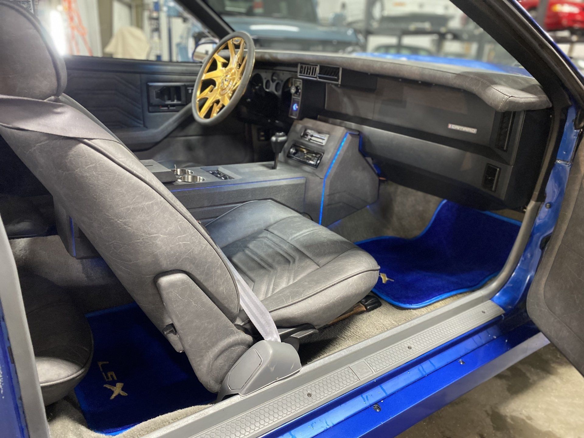 Blue custom car interior with black bucket seats, yellow steering wheel, and blue floor mats.