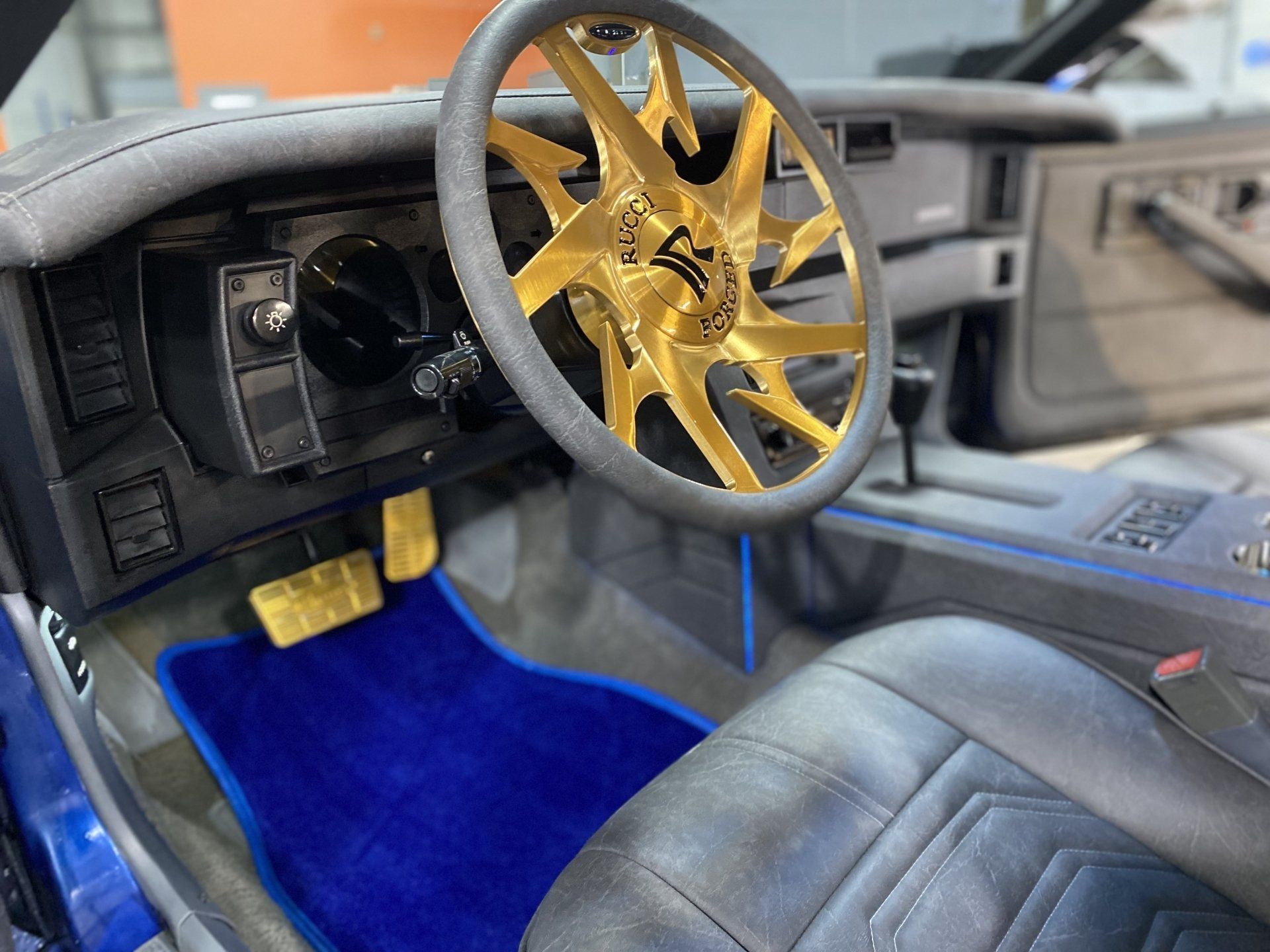 Custom car interior with gold steering wheel, blue carpet, and black leather seats.