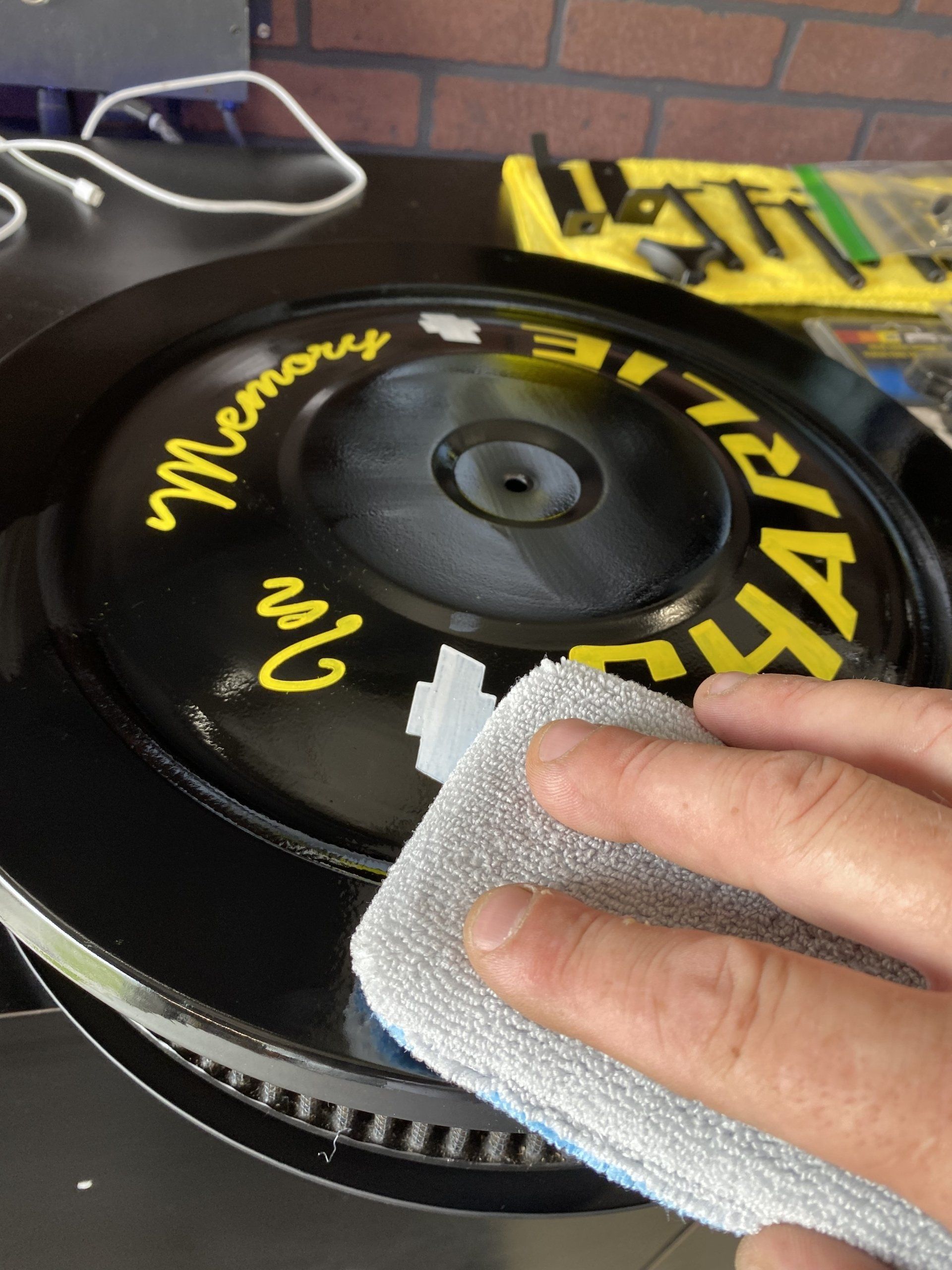 Hand cleaning a black turntable platter with a cloth; yellow lettering visible on the deck.