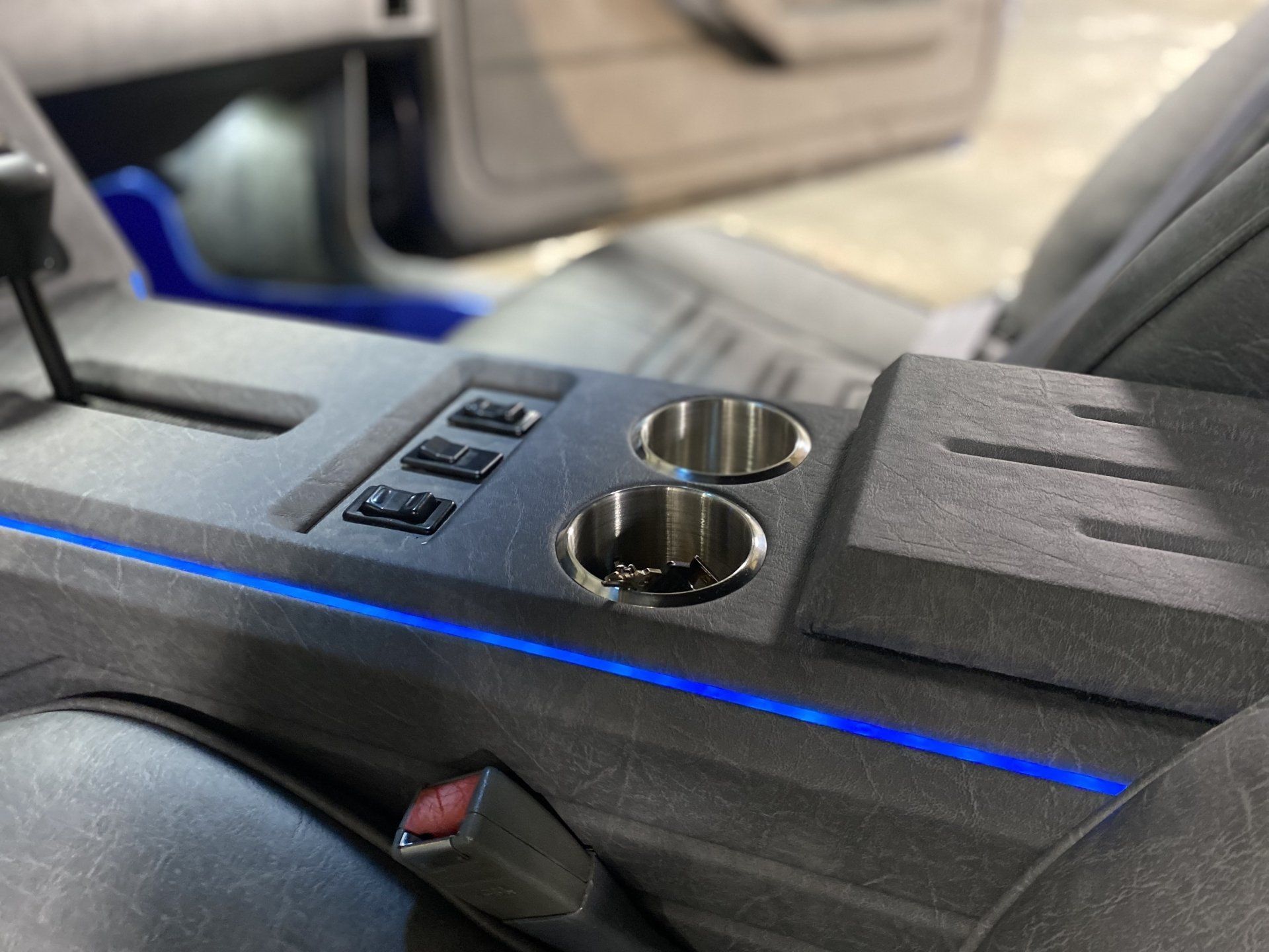 Car interior center console with two cup holders, window switches, and blue accent lighting.