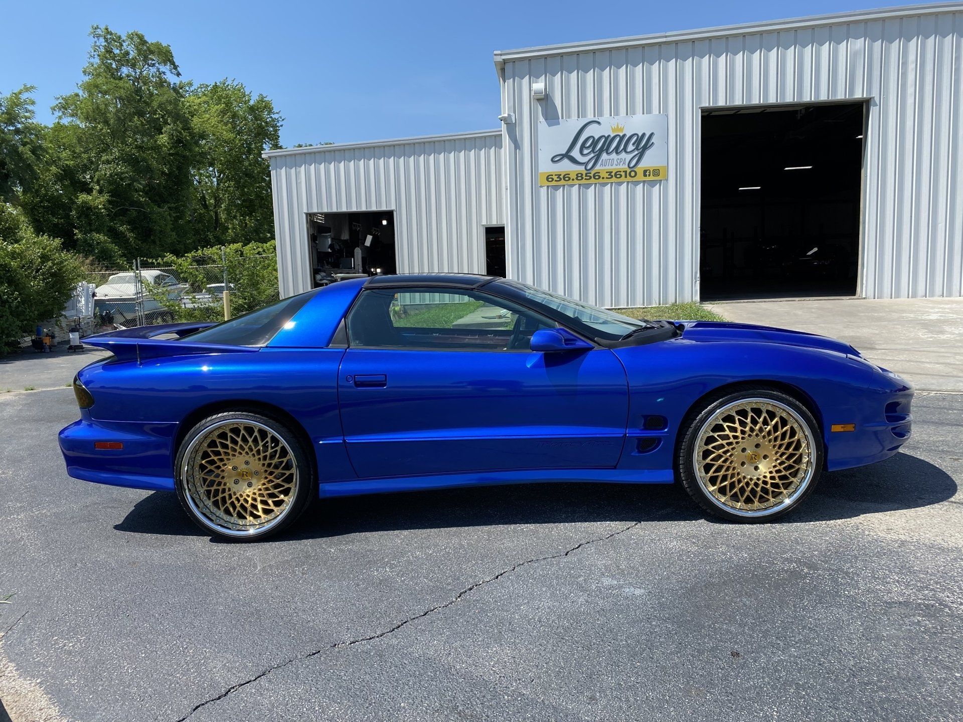 Blue sports coupe with gold wheels parked outside a white garage building
