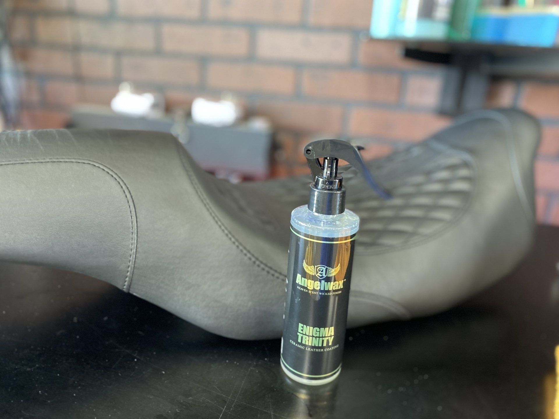 Black spray bottle on a bench seat with a motorcycle saddle in the background