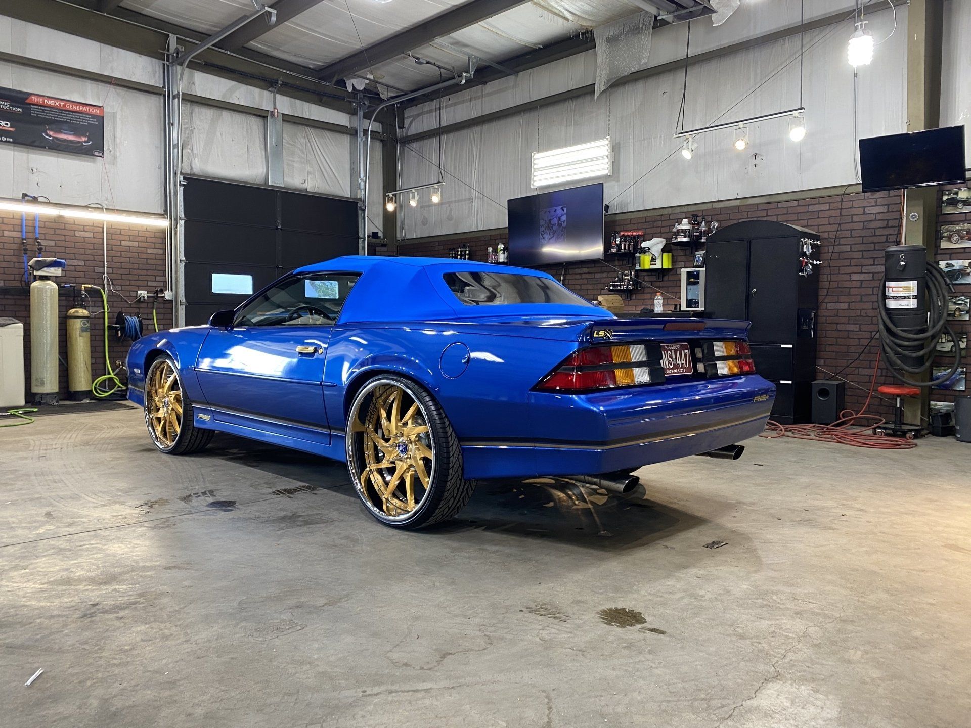 Blue sports car with gold rims parked inside an auto shop garage