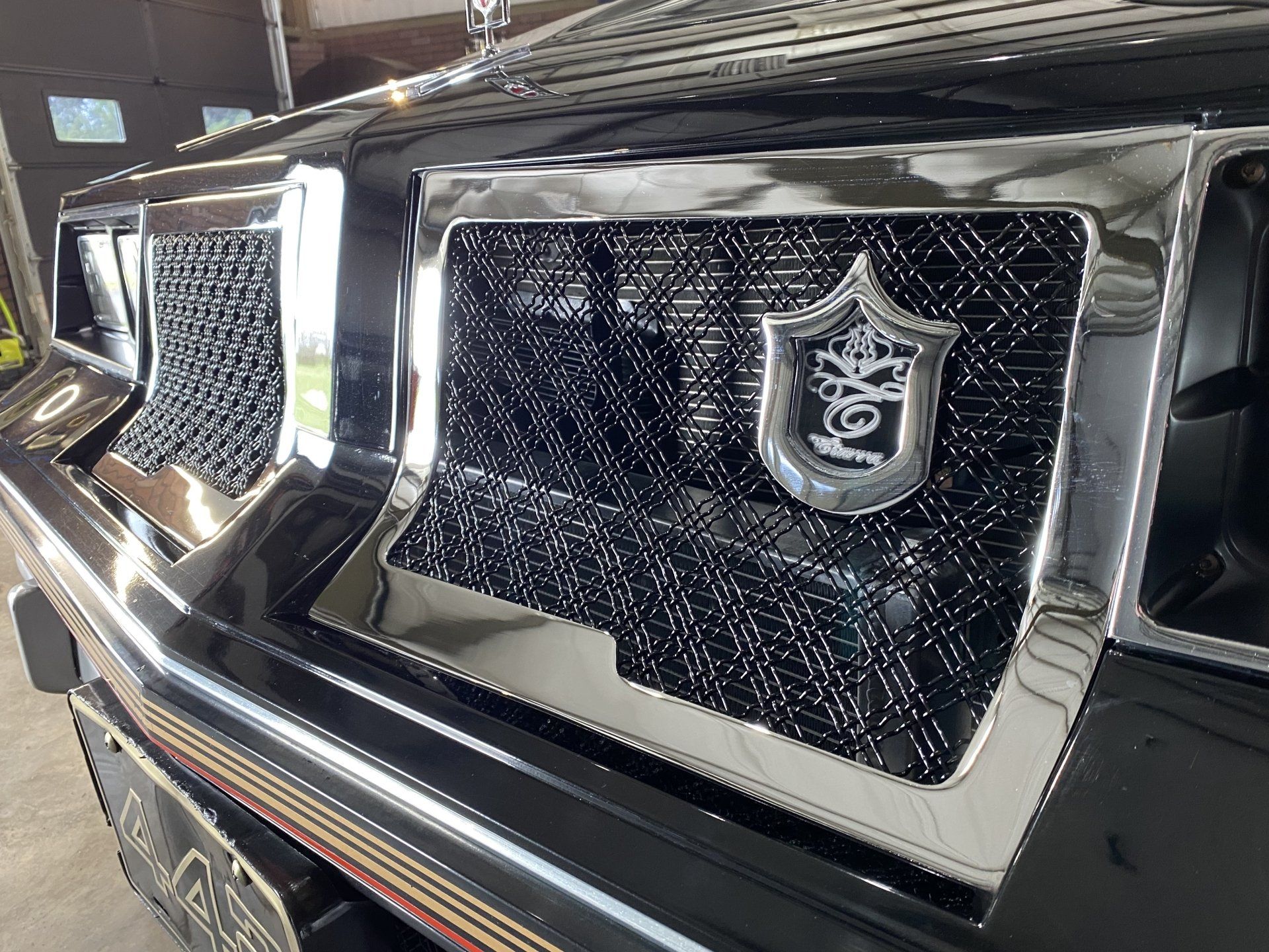 Chrome car grille with a black mesh insert and a shield emblem on a glossy black vehicle front