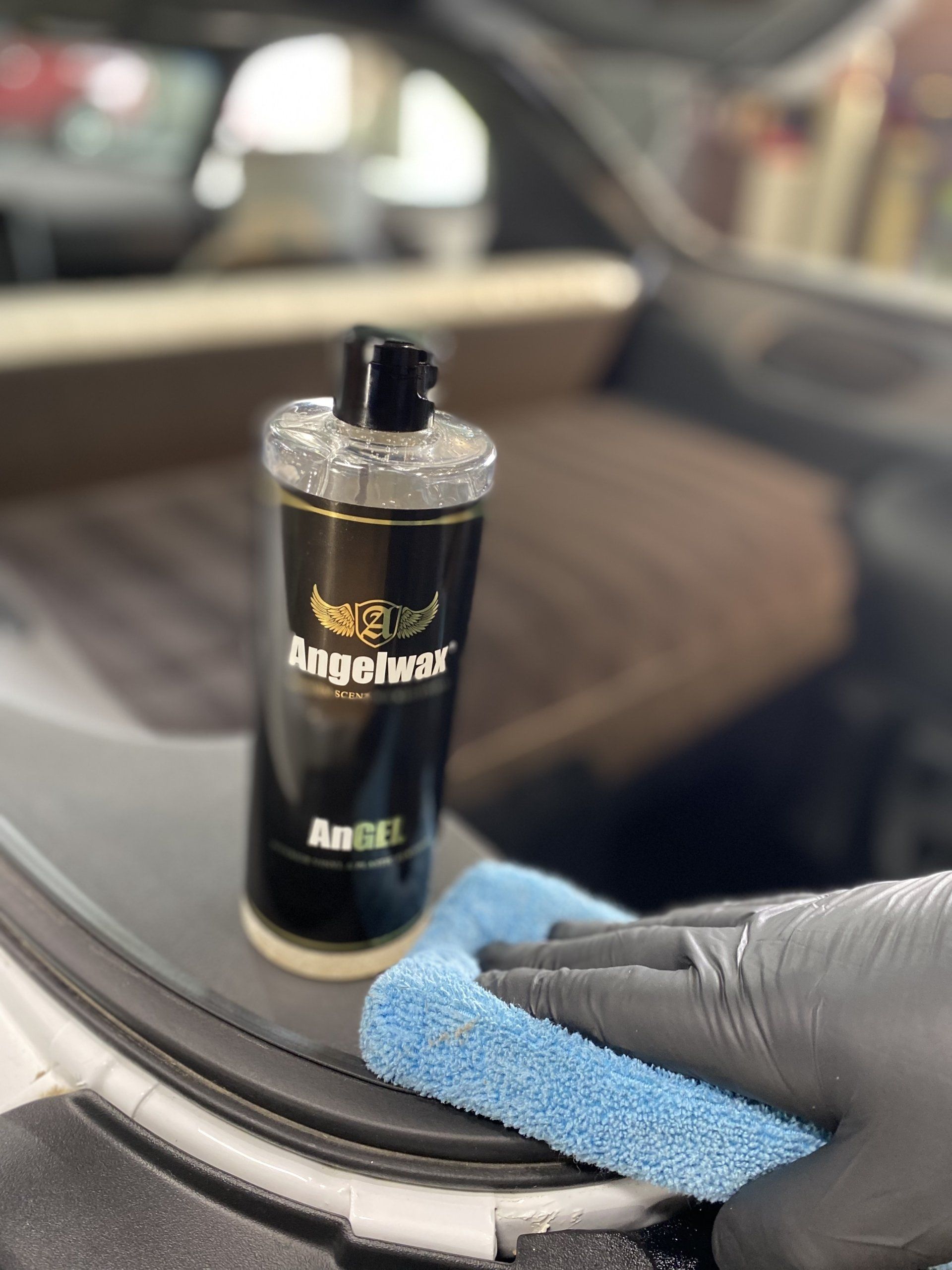 Black bottle on a car dashboard being wiped with a blue cloth by a gloved hand.