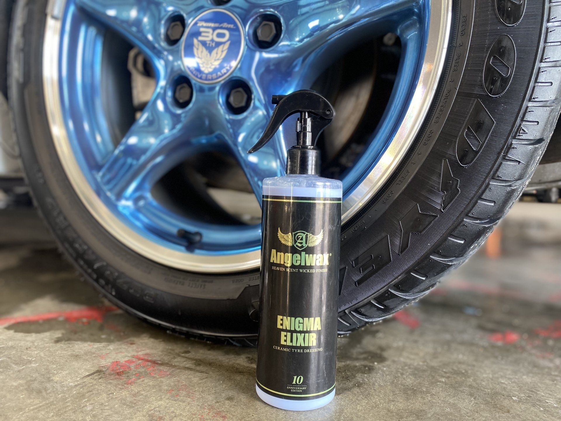 Black tire cleaner bottle in front of a blue car wheel on a garage floor