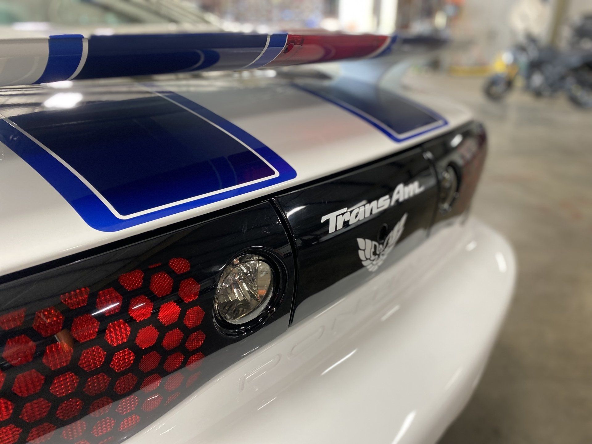 Close-up of a black race car tail with blue stripes, red taillights, and a wing spoiler in a garage