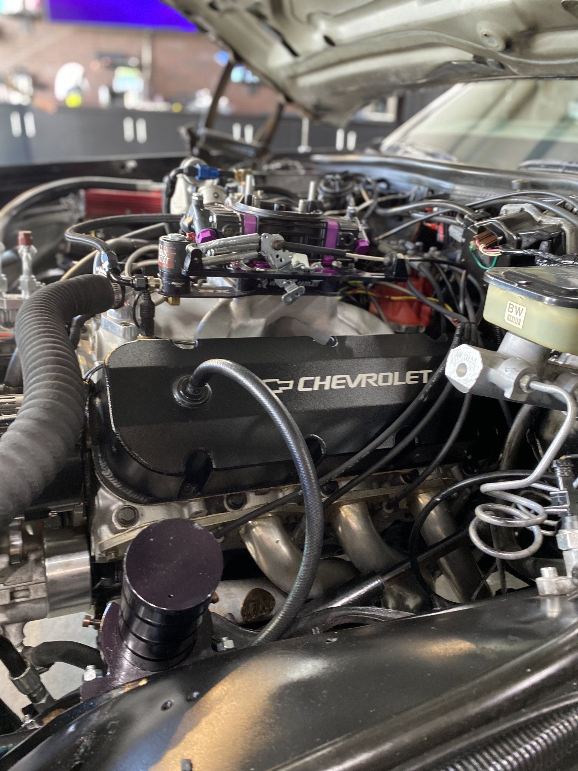 Close-up of a Chevrolet engine in a car bay, with hoses, wiring, and open hood visible
