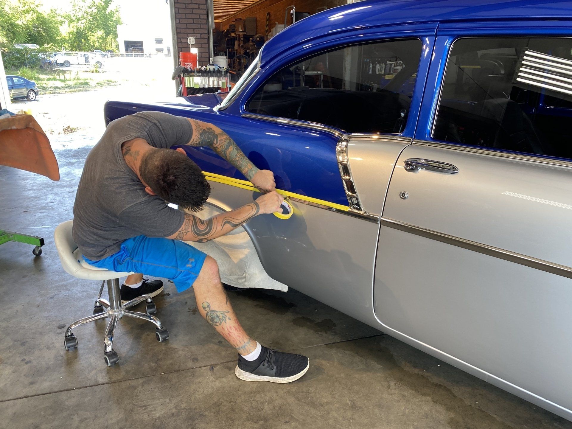 Person uses a squeegee on a blue-and-silver car inside a garage.