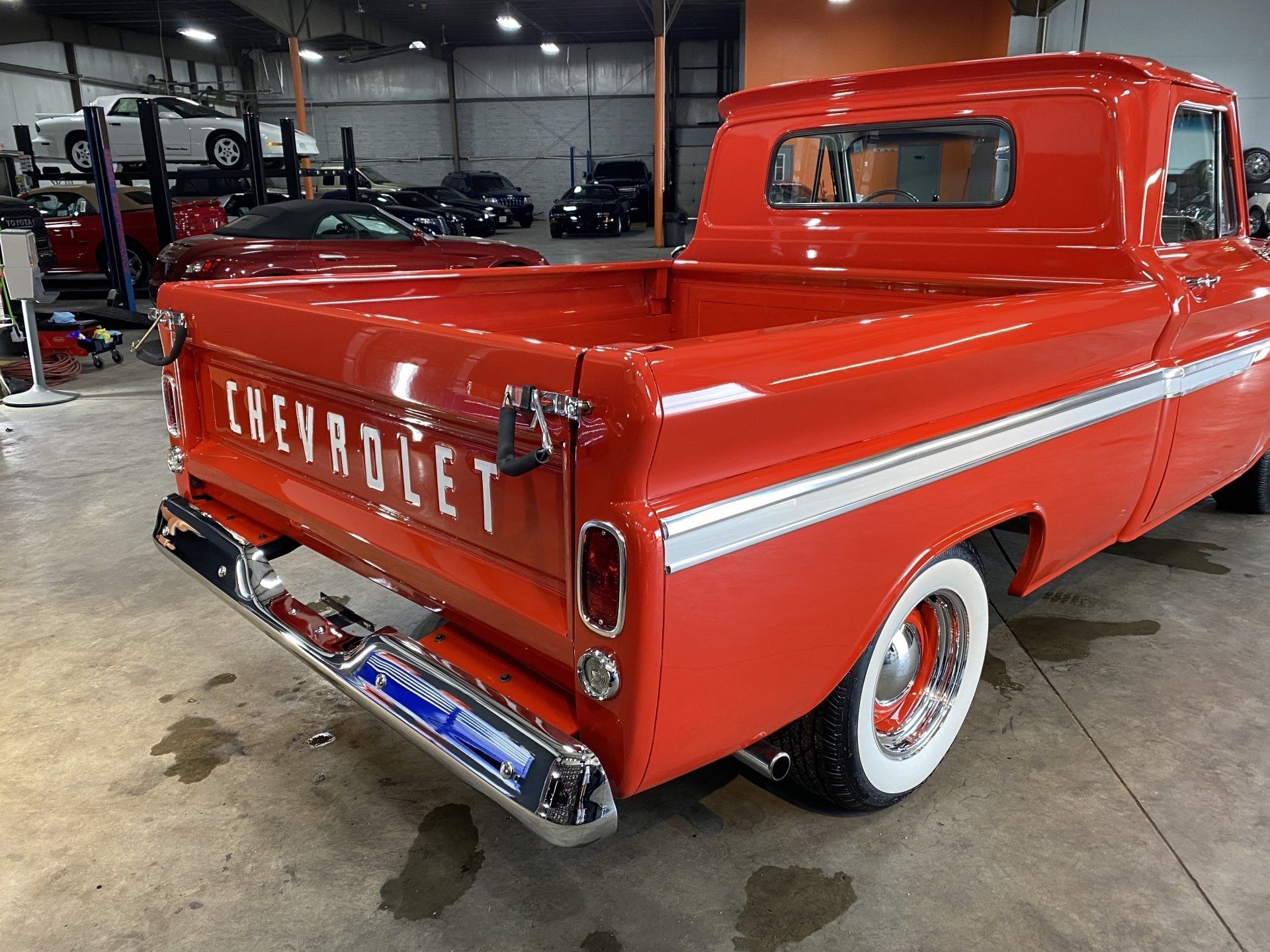 Red Chevrolet pickup truck with whitewall tires parked in a garage, rear three-quarter view.