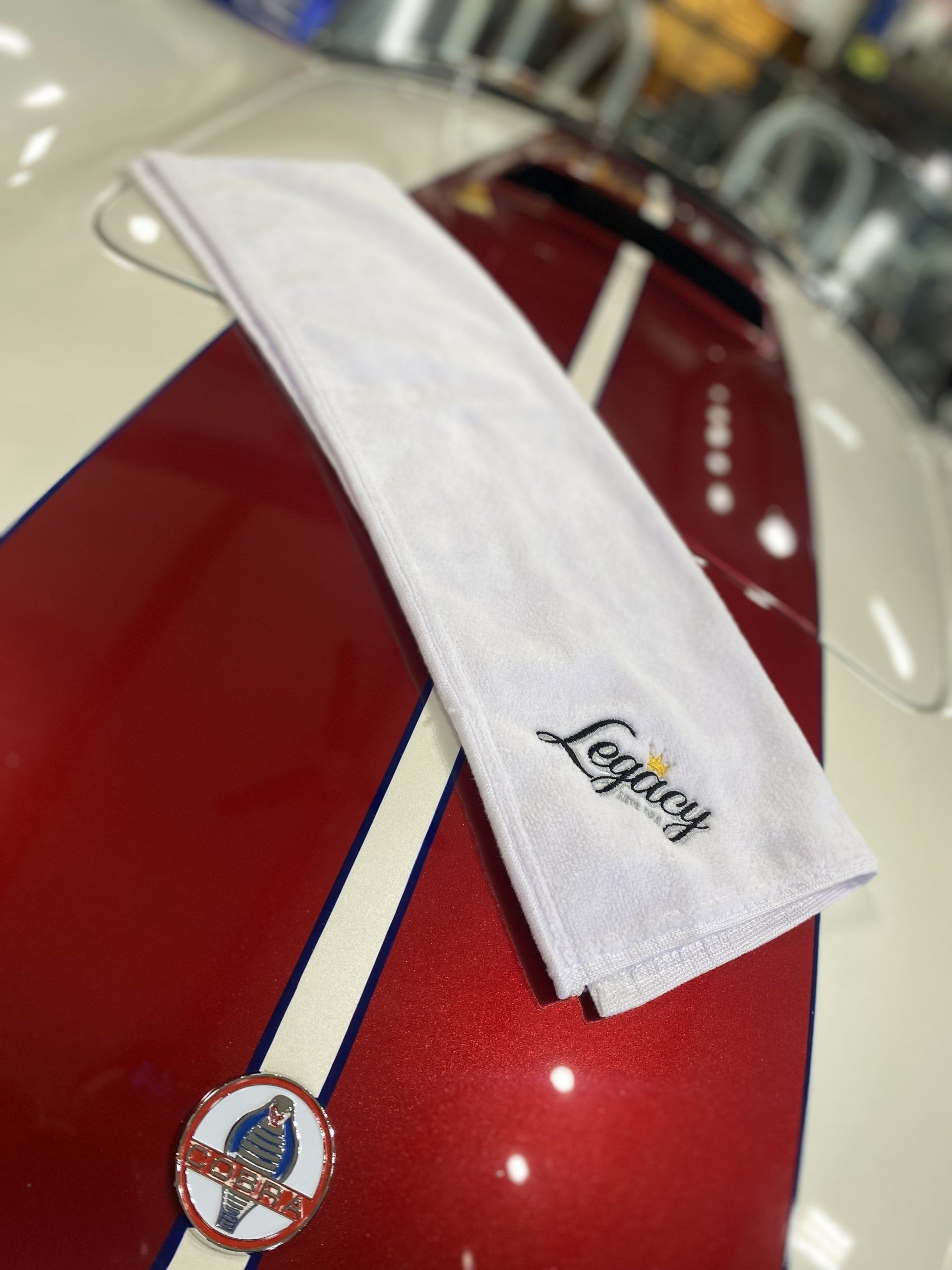 White towel draped over a glossy red car hood with a circular emblem and stripe detail