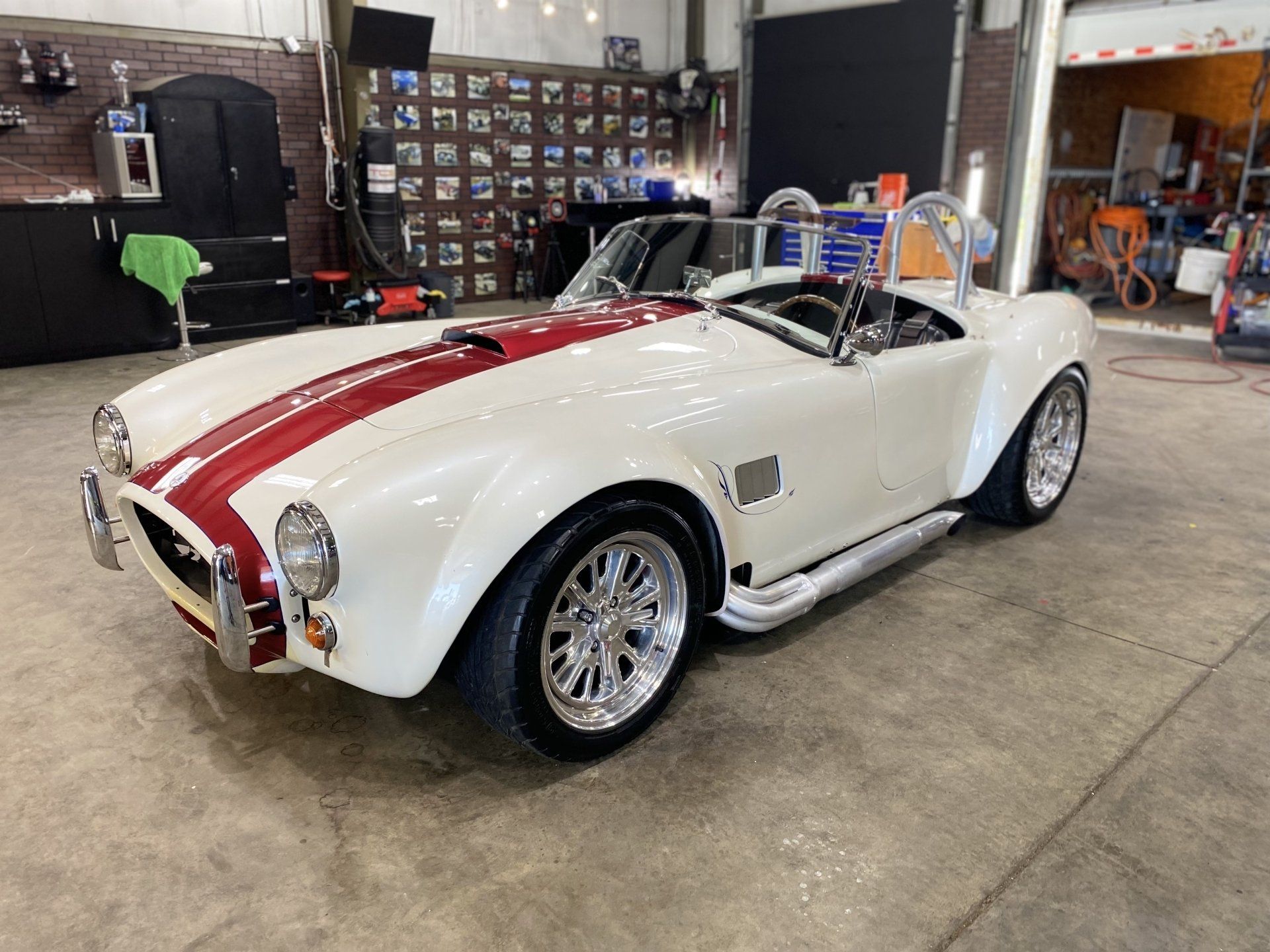 White classic sports car with red racing stripes parked indoors in a garage