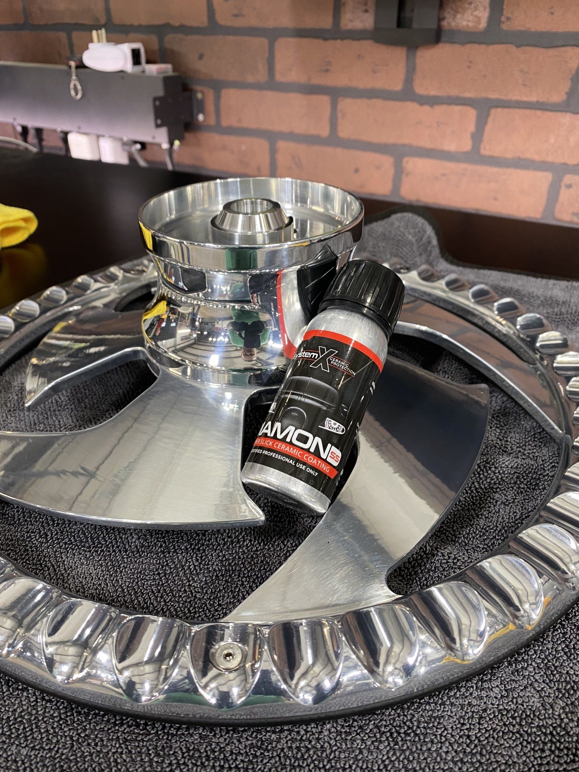 Chrome hookah tray with a black cleaning brush on it, against a brick wall.