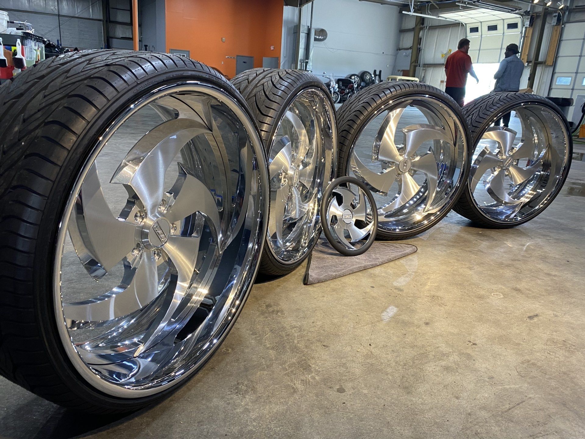 Custom chrome car wheels lined up in a garage, with one mounted tire in the foreground.