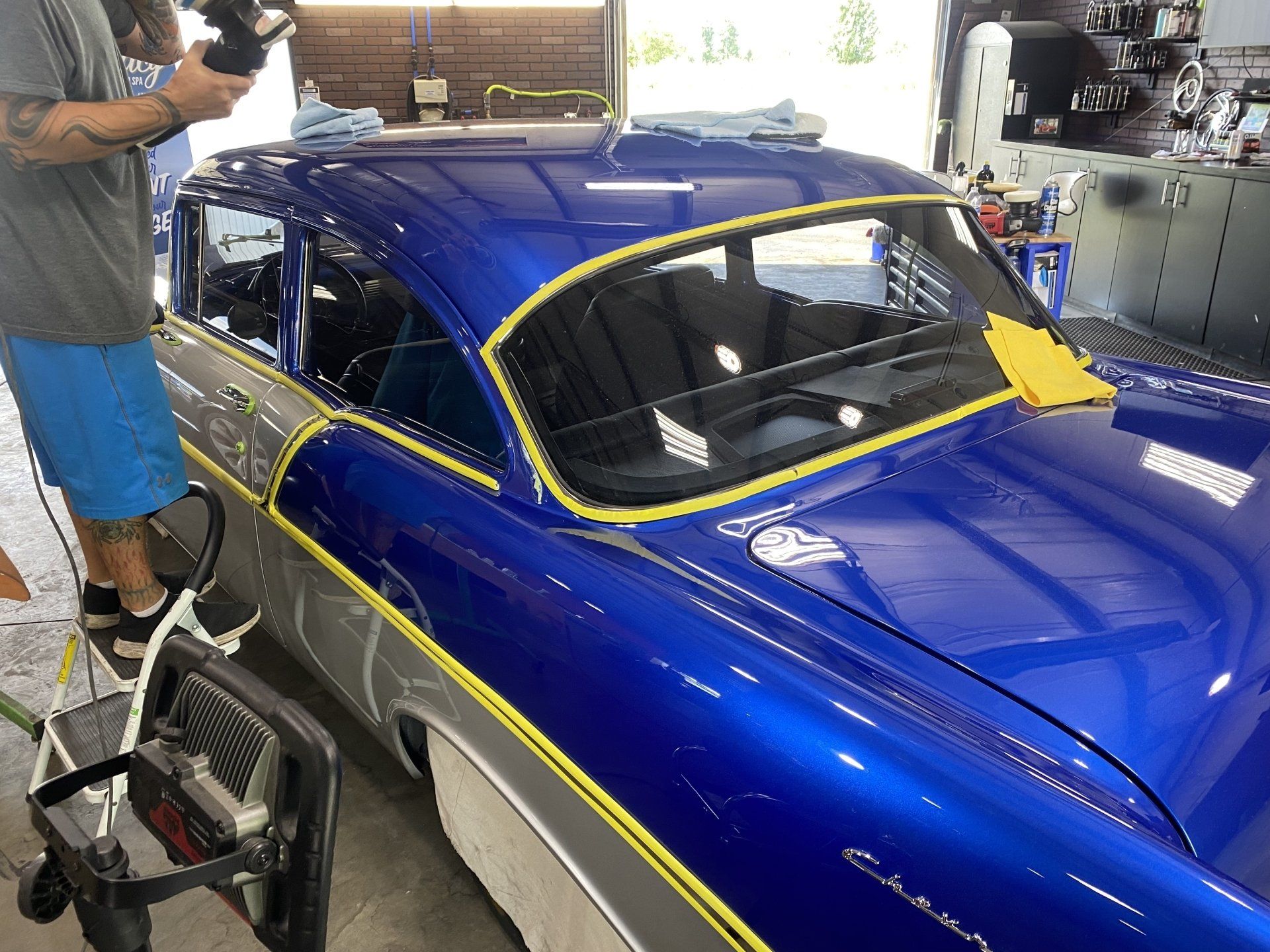 Blue race car being wrapped in yellow tape inside a garage, with a person standing beside it.