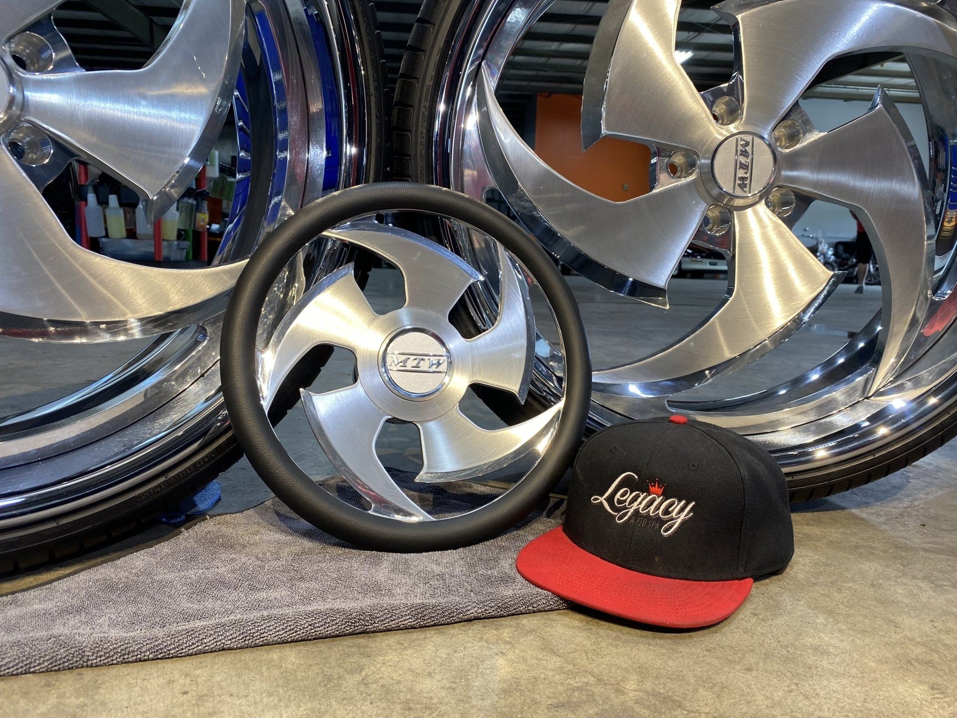 Custom chrome car wheels and a black-and-red cap displayed on a gray carpet.