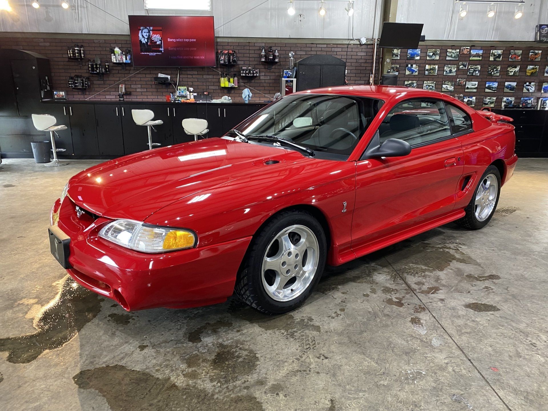 Red sports coupe in a showroom, glossy paint with a wet floor reflecting the car.