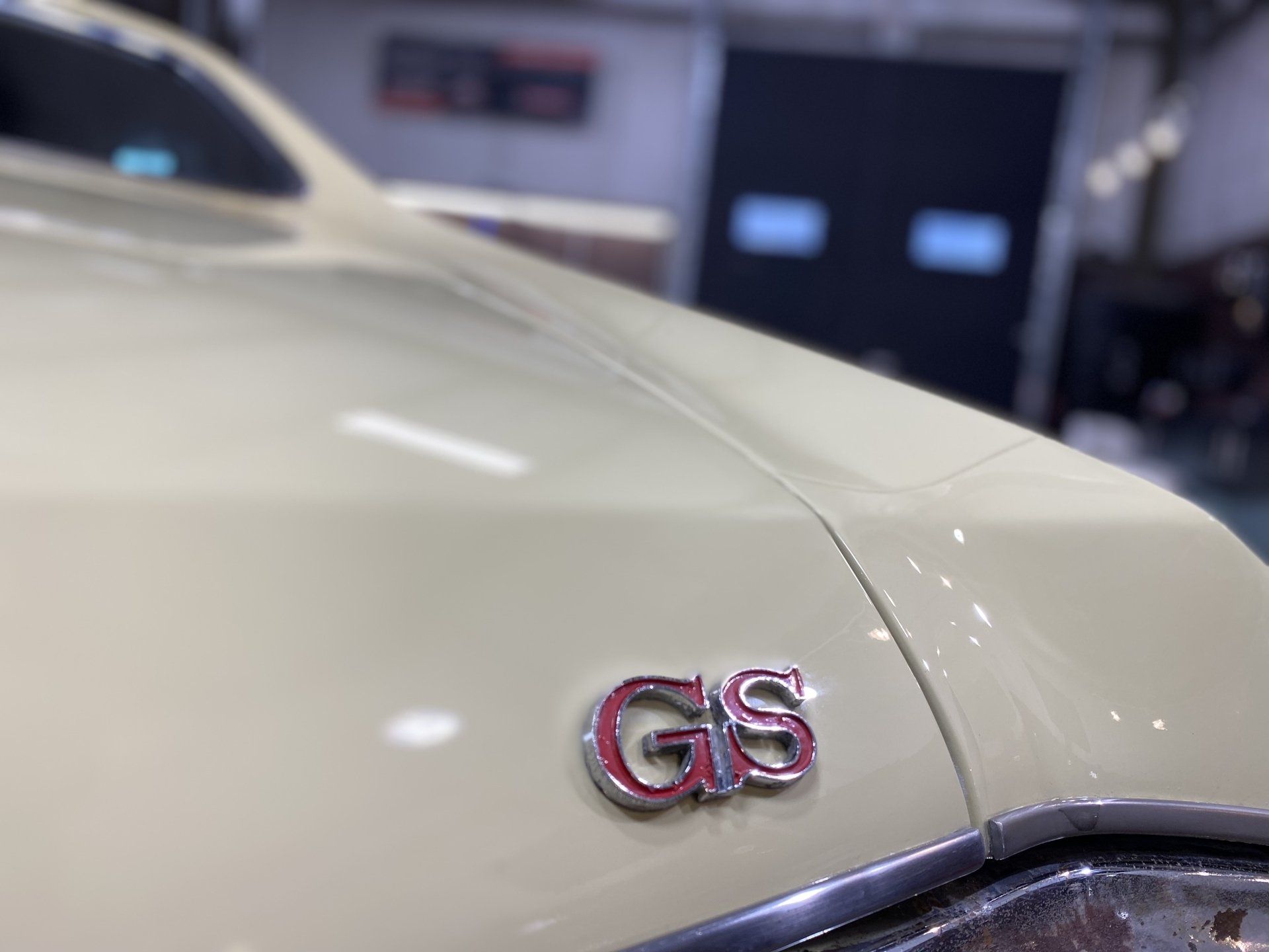 Close-up of a white car’s front fender with a pink-and-chrome GS badge