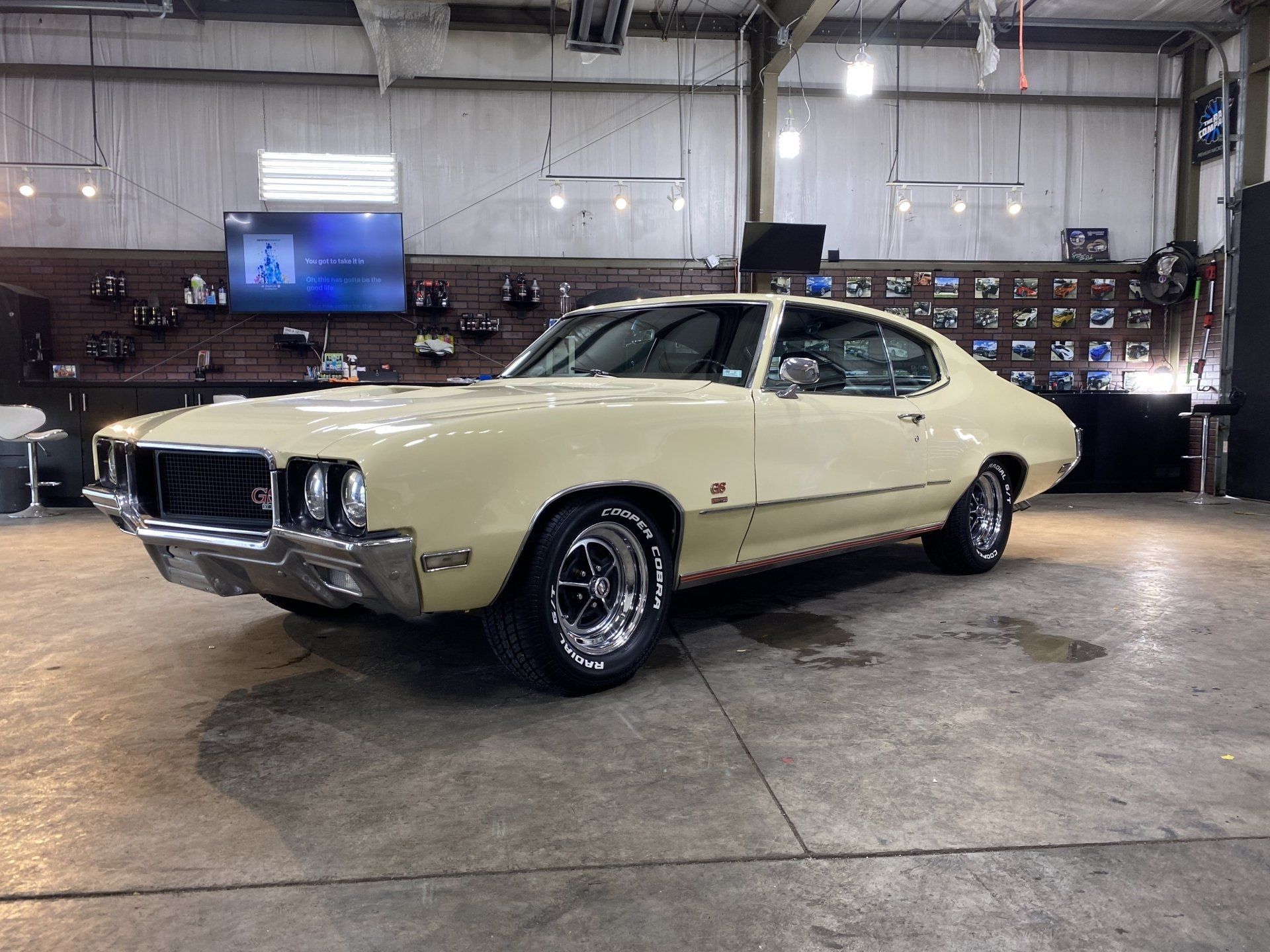 Cream-colored classic coupe in a garage, shown in three-quarter view on a polished concrete floor.