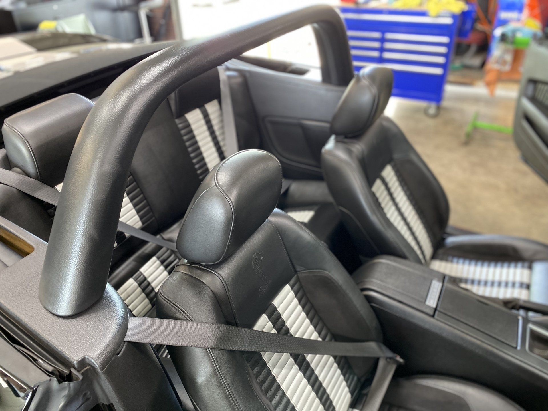Two black car seats with harnesses, shown in a garage or workshop setting.