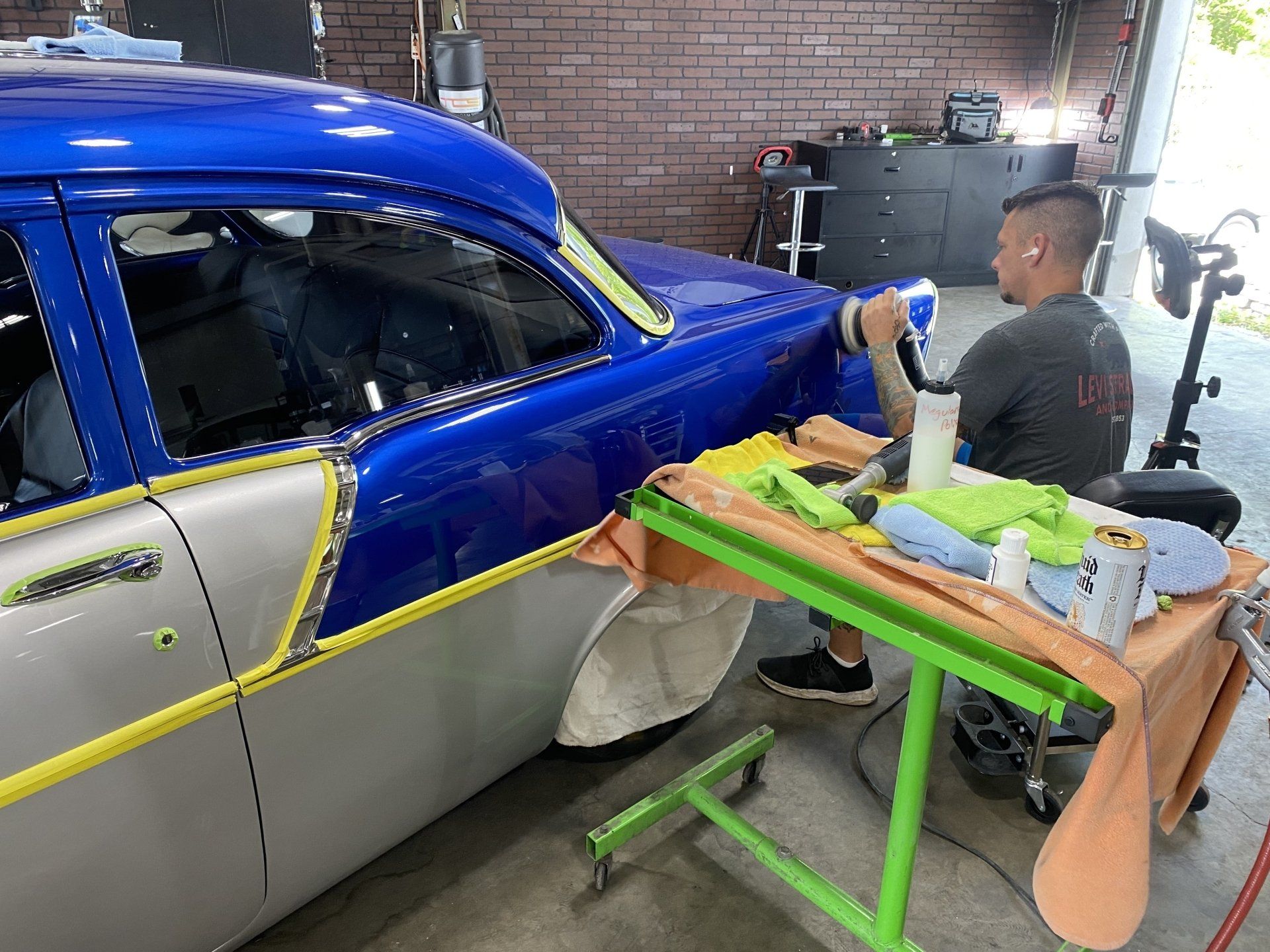 Person spray-painting a blue-and-silver car body in a garage workshop