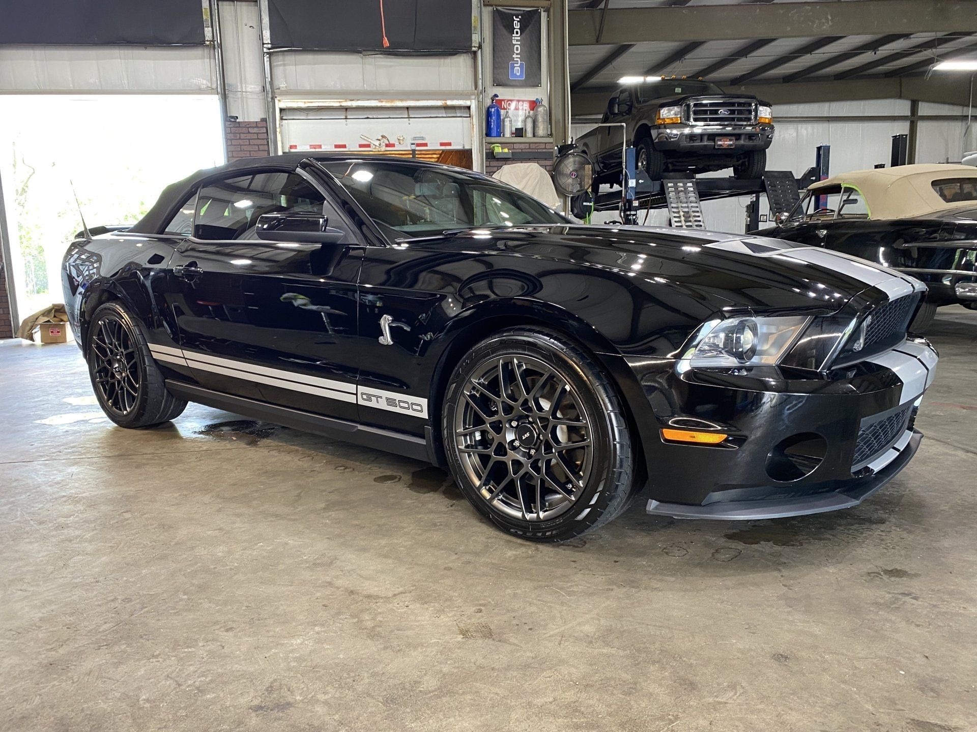 Black sports car in a garage, side view with shiny rims and racing stripes