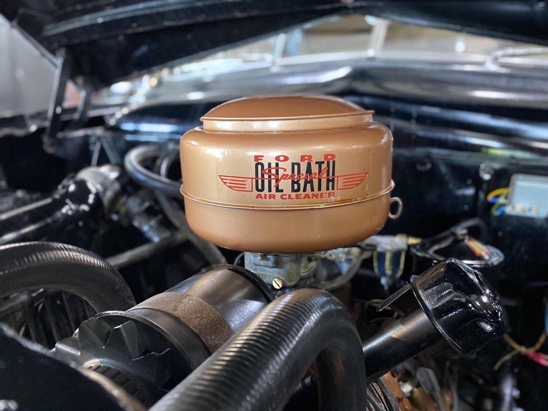 Tan air filter on a car engine, labeled “BILATA” with red wings, among black hoses.