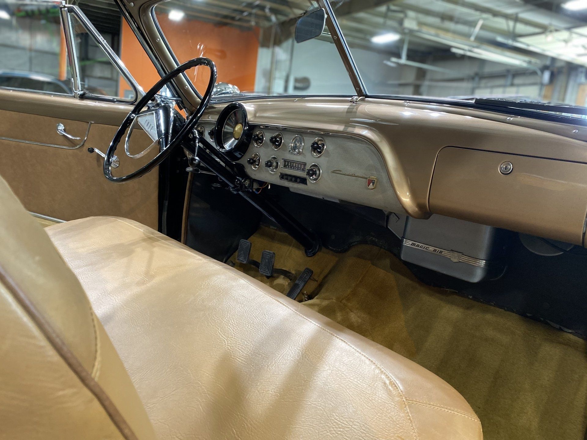 Interior of a vintage car with tan seats, black steering wheel, and beige dashboard