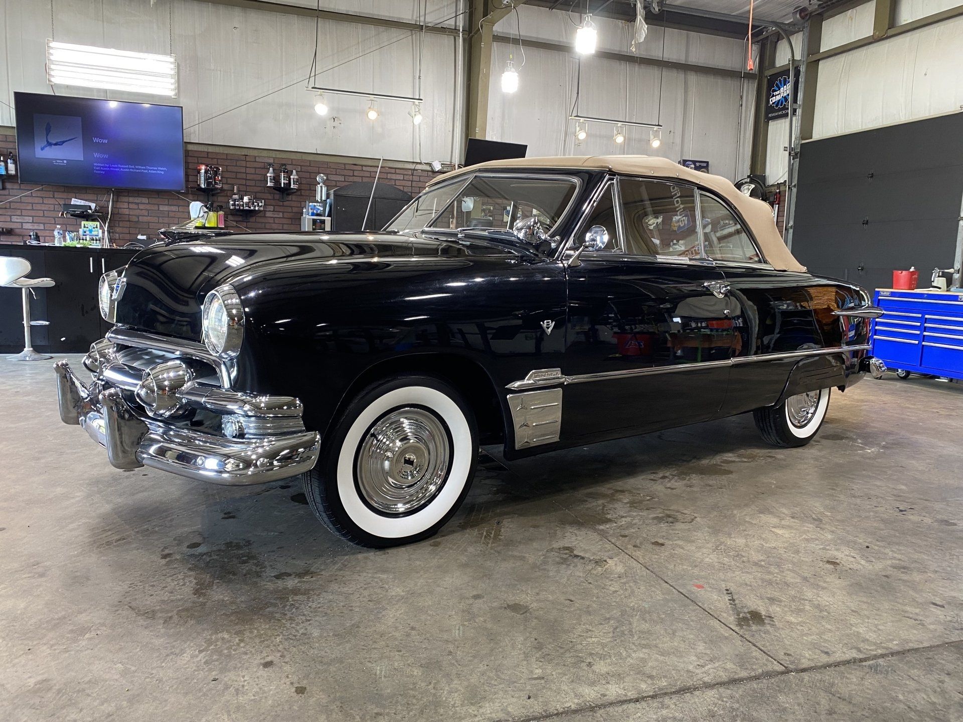Black vintage car with whitewall tires parked inside an auto garage, front angled view