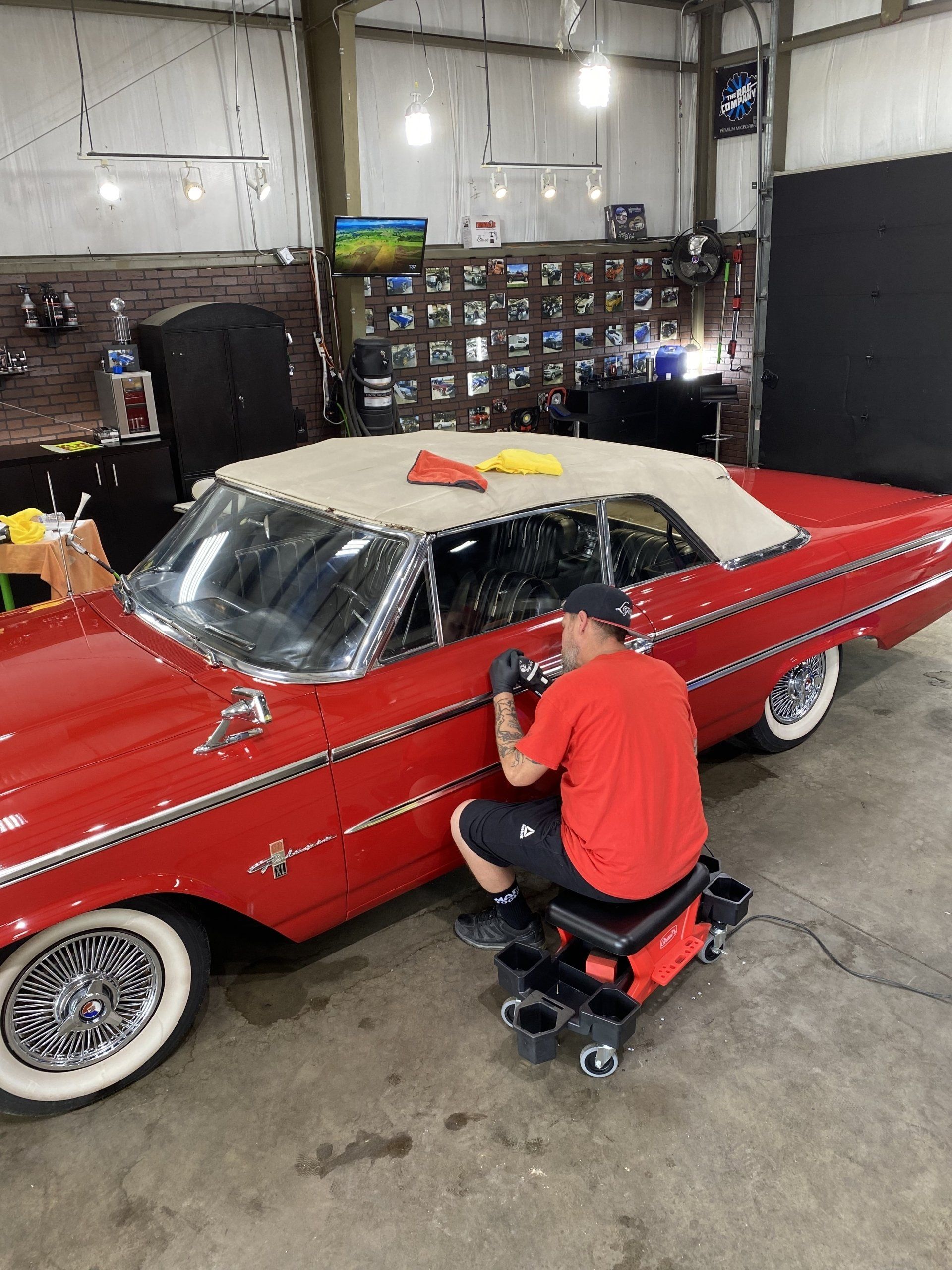 Person working on a red classic convertible inside a garage
