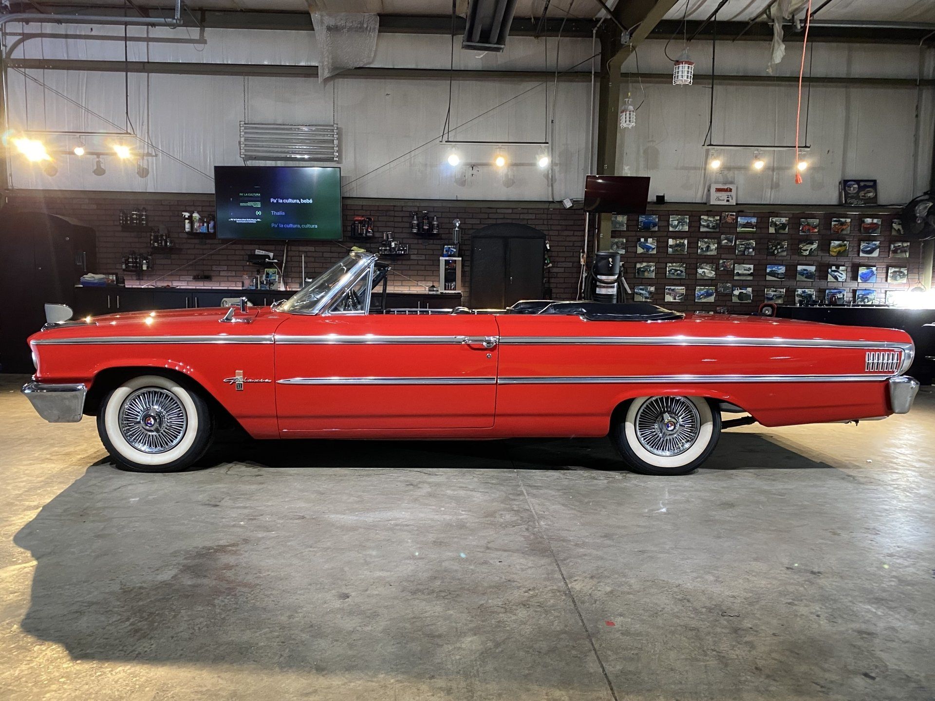 Red classic convertible lowrider in a garage, side view, with chrome trim and whitewall tires