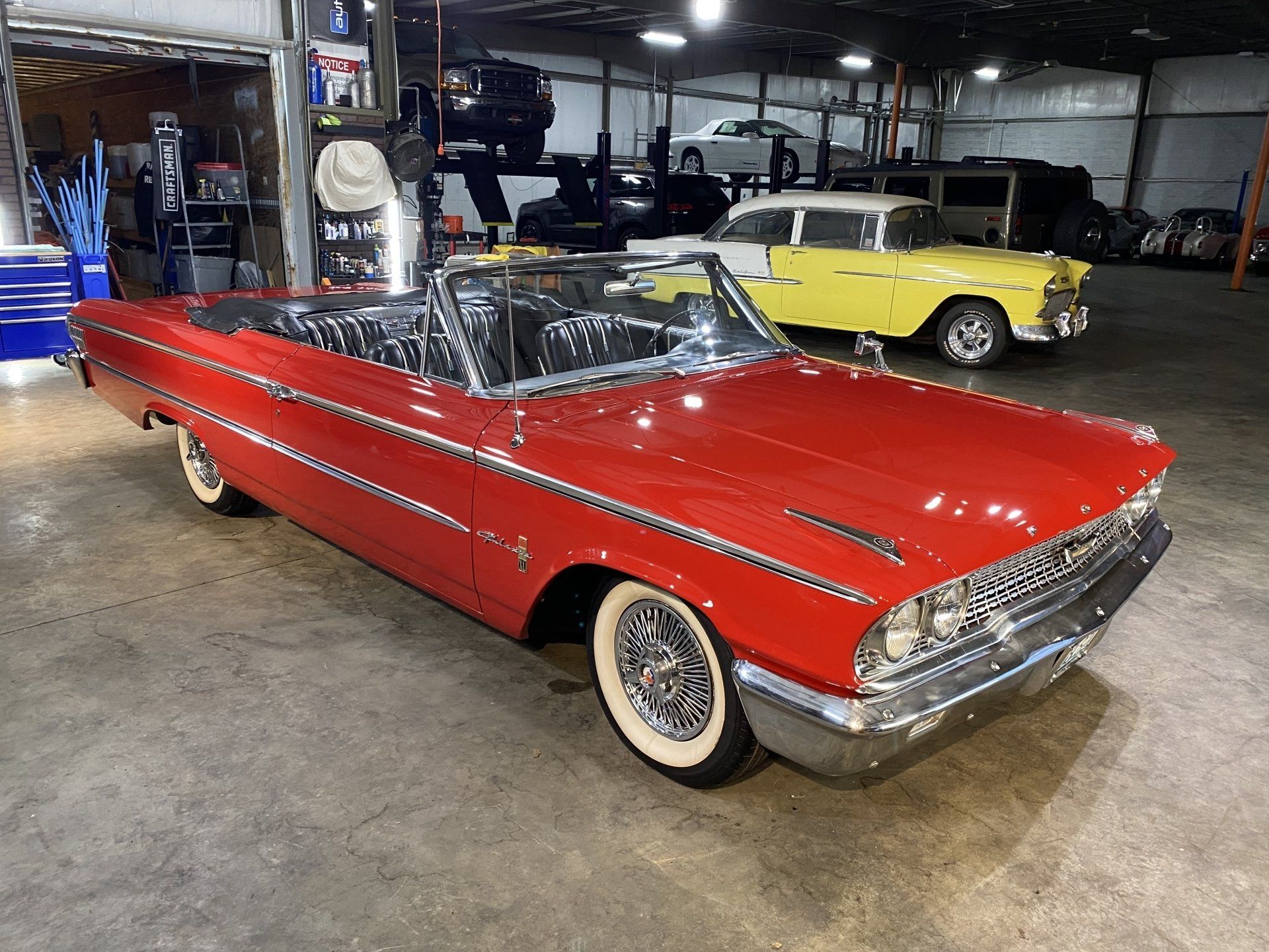 Red classic convertible in a garage showroom, with a yellow vintage car in the background