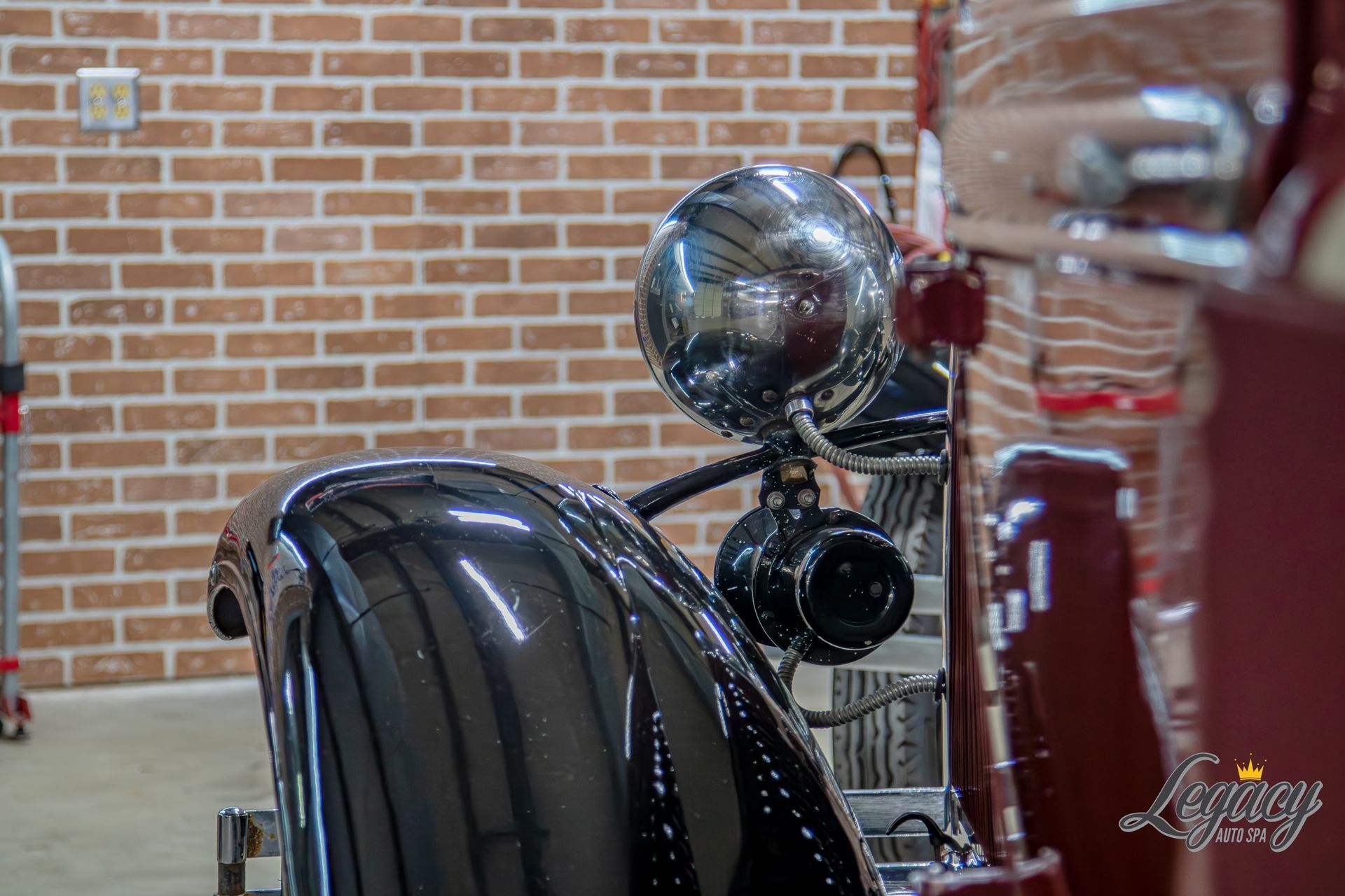 Vintage black car front end with chrome headlight and glossy fender against a brick wall