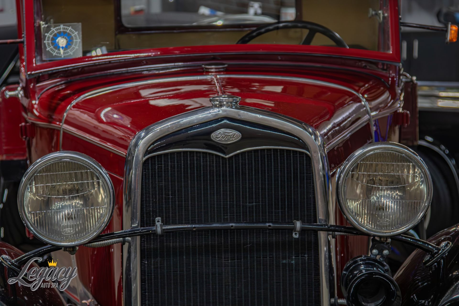 Front view of a shiny red vintage car with chrome grille and round headlights
