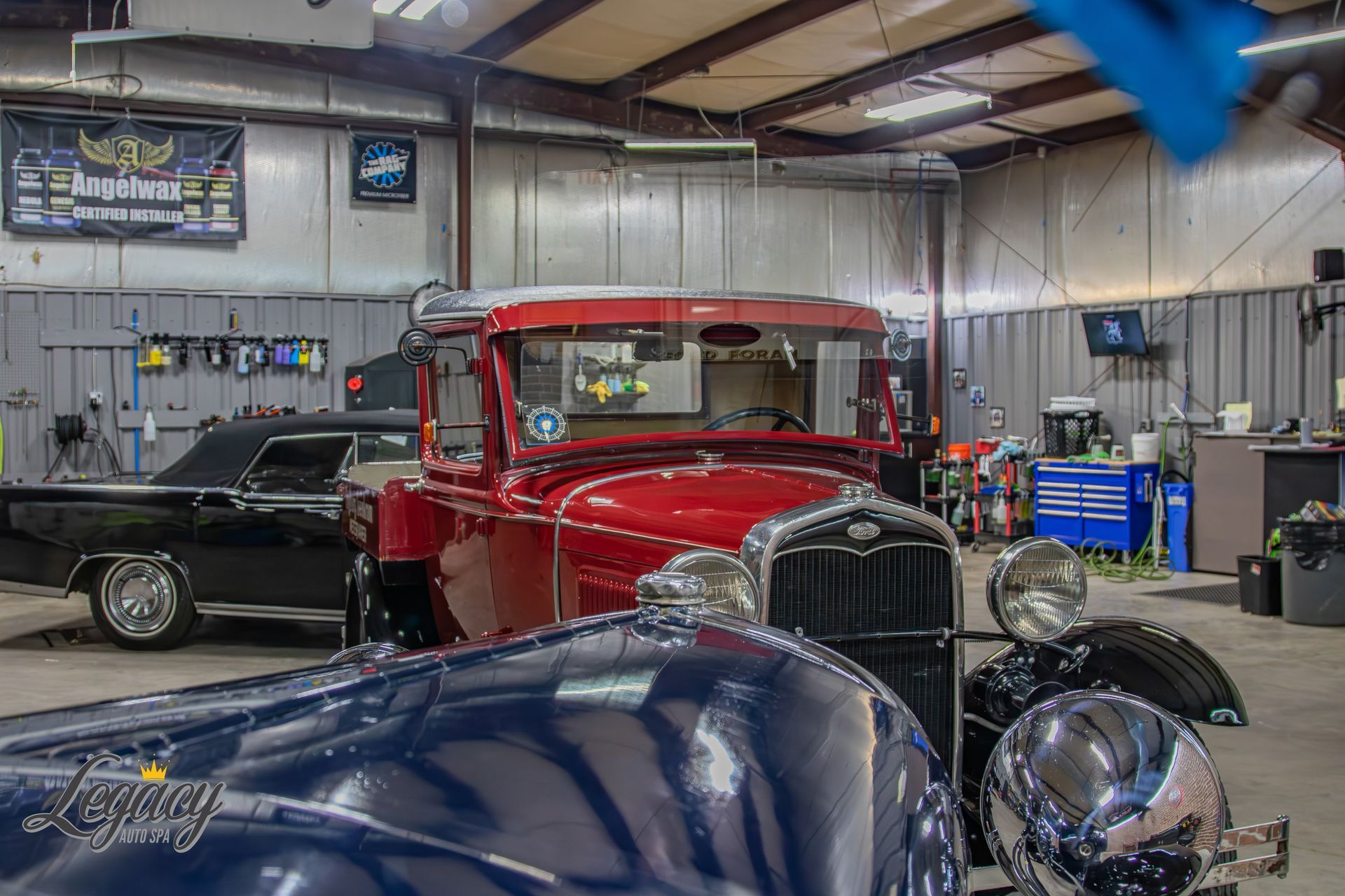 Classic cars in a garage, including a red hot rod and a blue car in the foreground.