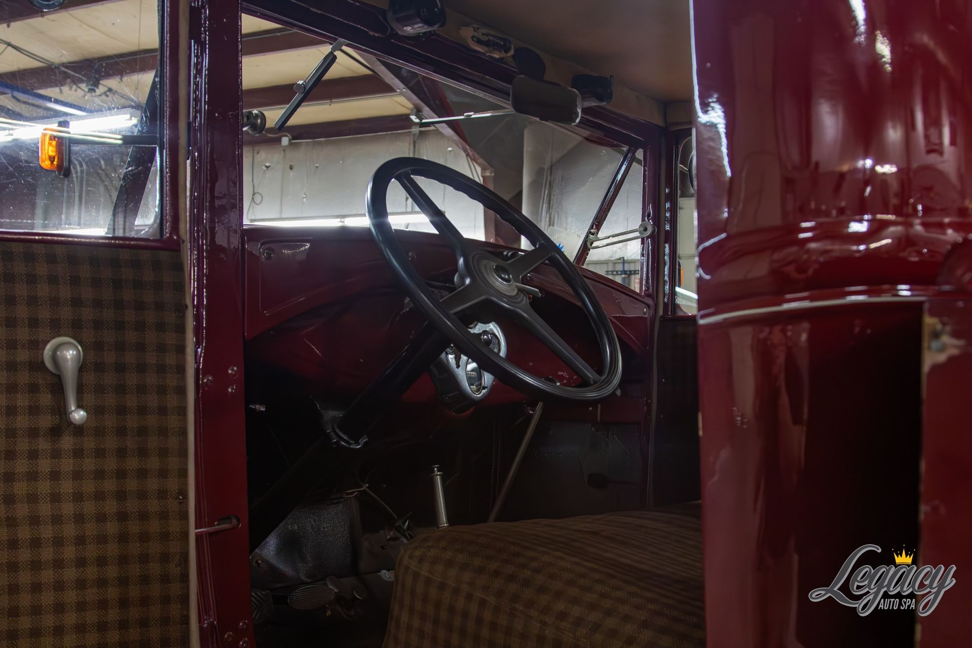 Interior of a maroon vintage car with a black steering wheel and plaid upholstery