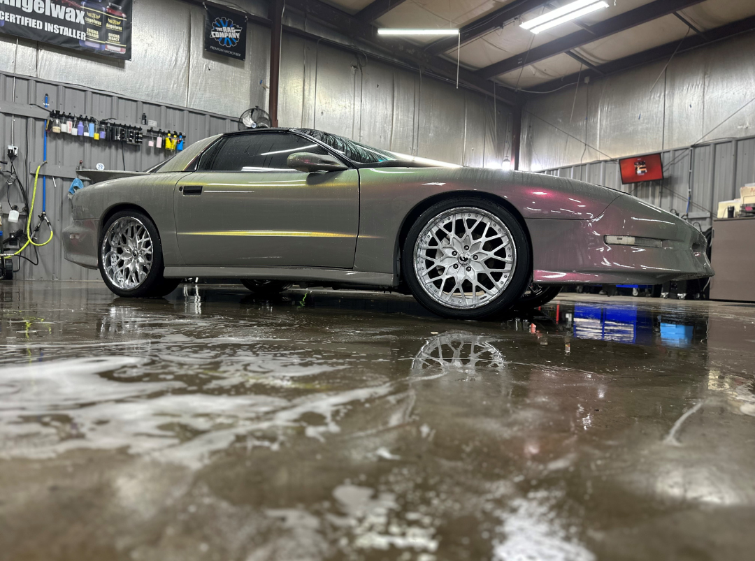 Silver sports car in a wet garage, low side view with reflections on the floor.