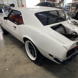 White classic muscle car with exposed rear engine, parked indoors in a garage