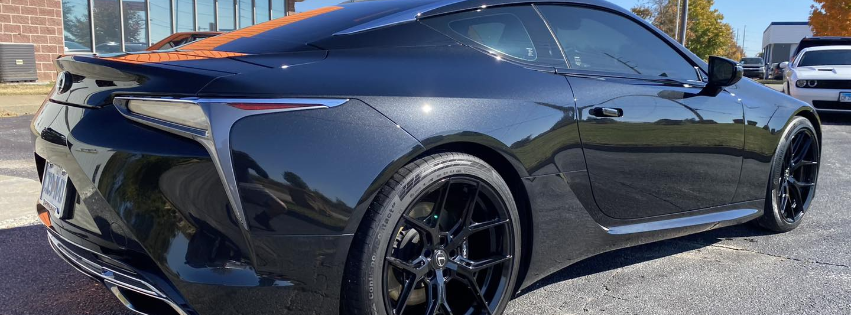 Black sports coupe parked outdoors in sunlight, side view with glossy paint and tinted windows