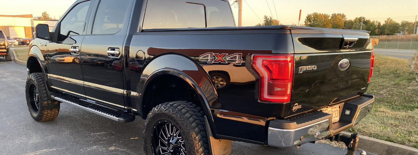 Black lifted pickup truck parked on a road at sunset, rear three-quarter view