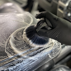 Gloved hand washing a car wheel with foamy soap in a detailing bay