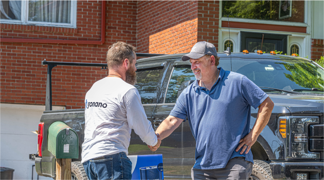 Two men shaking hands in front of a brick house and black pickup truck.