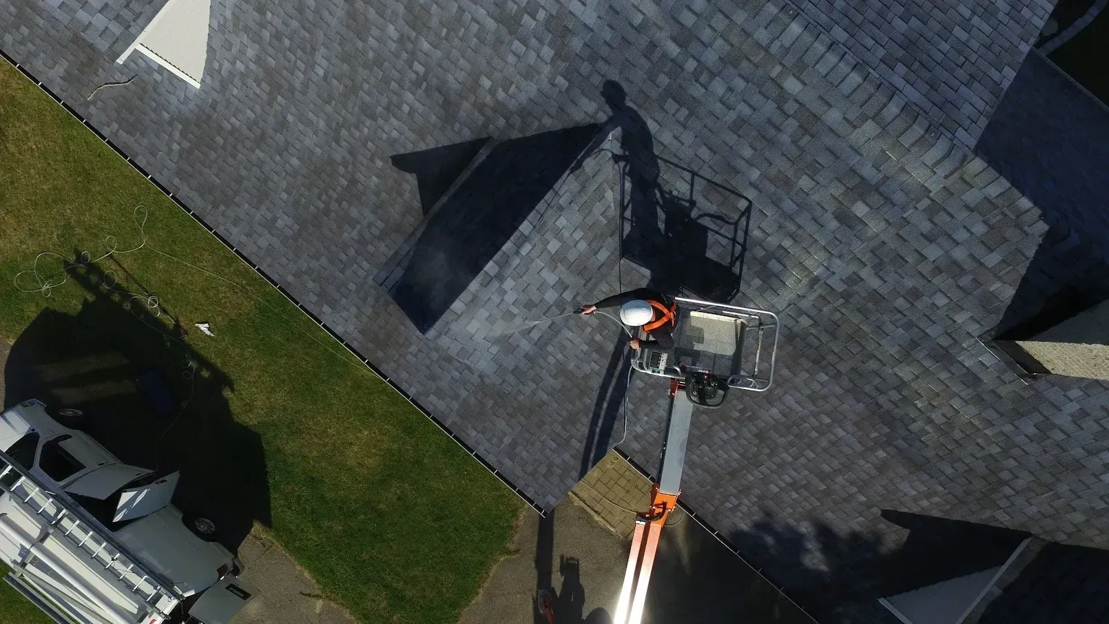 Aerial view of a rooftop with a worker on a lift beside solar panels and shadows on gray shingles