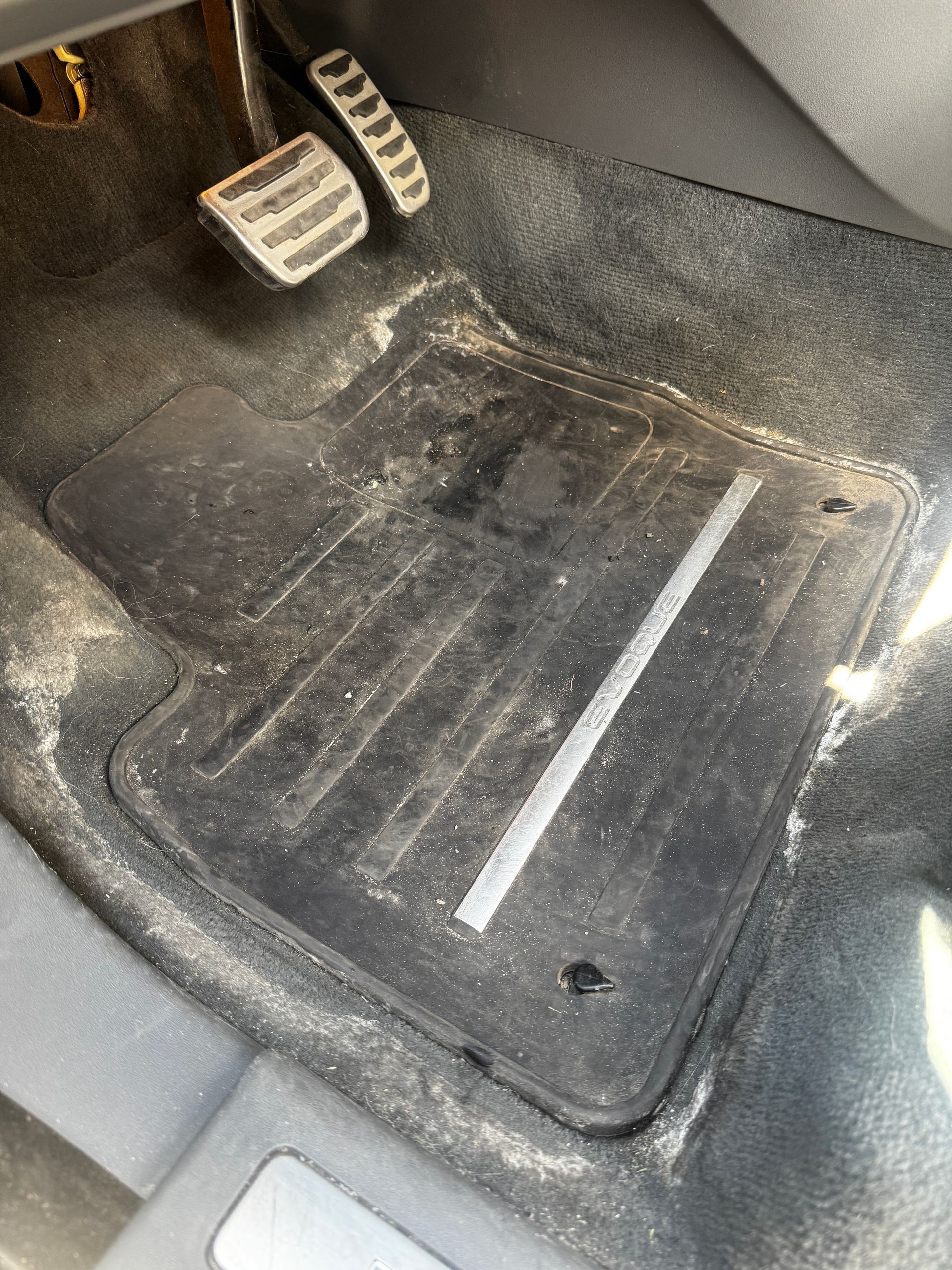Car floor mat with dirt and debris beneath the pedals in the driver’s footwell