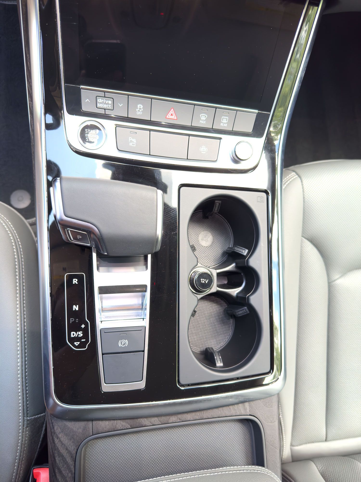Car center console with touchscreen controls, gear selector, and dual cup holders in a dark interior