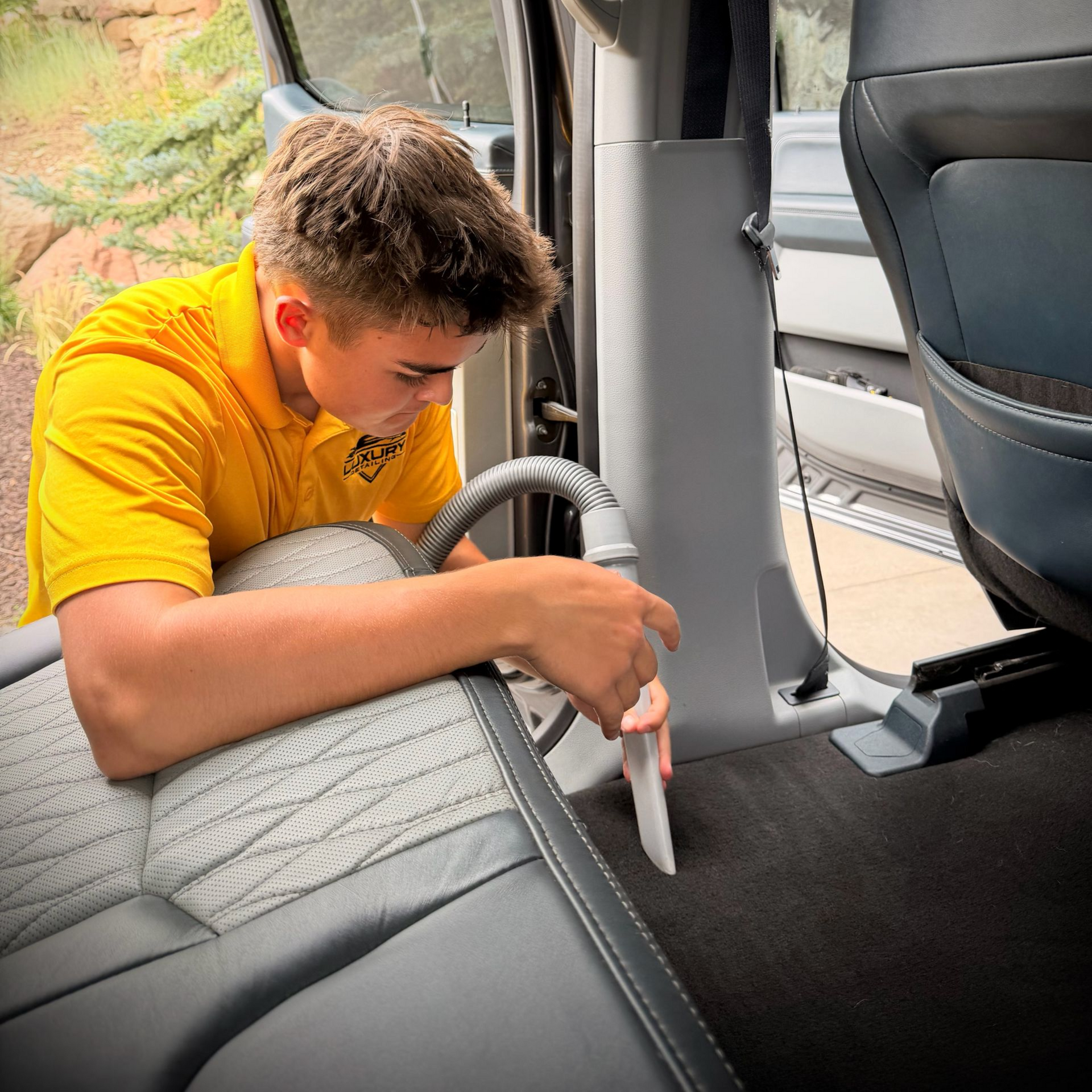 Person in a yellow shirt cleaning the back seat of a car with the door open.