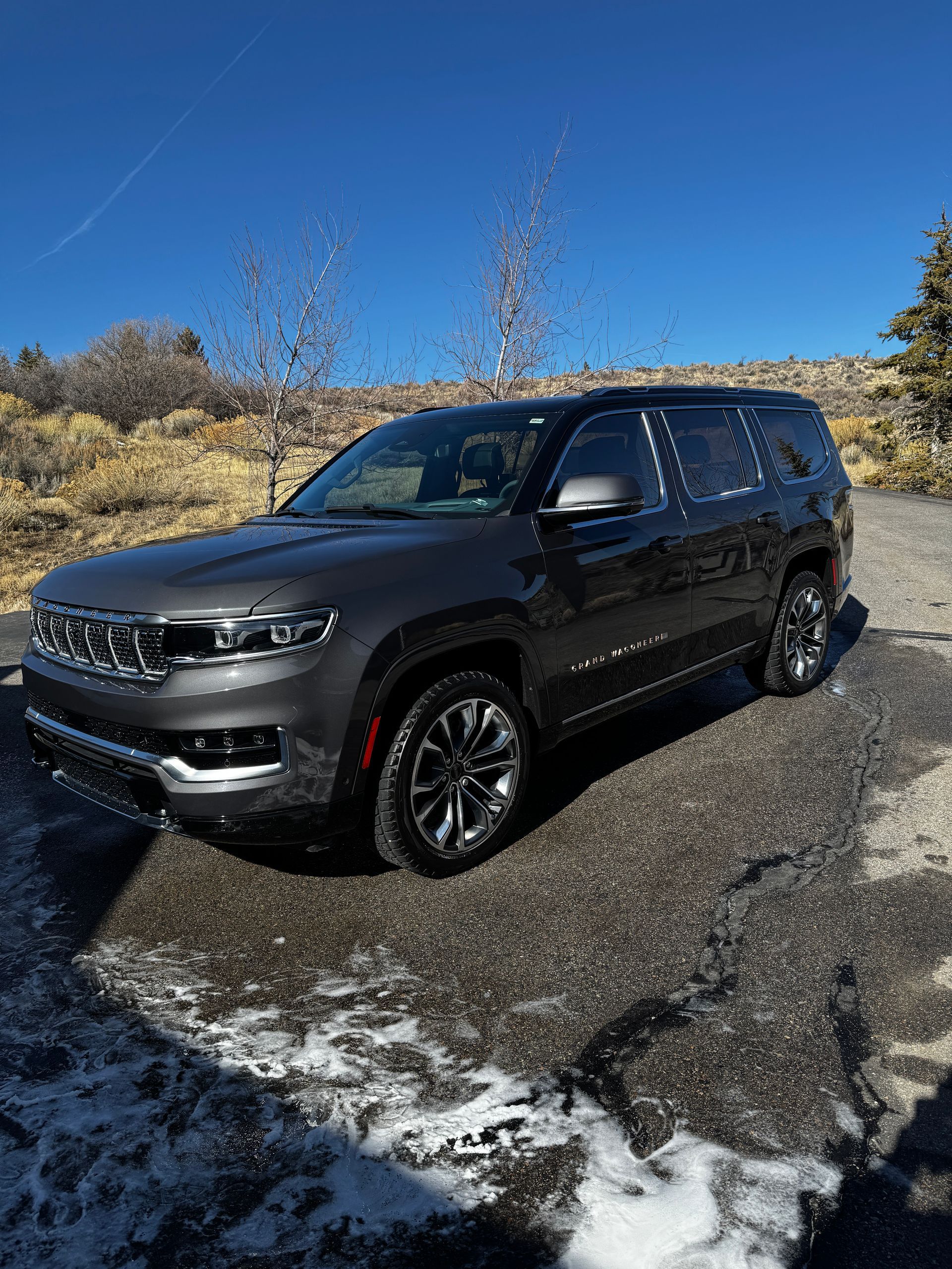 Black SUV parked on a gravel lot with snow patches under a clear blue sky.