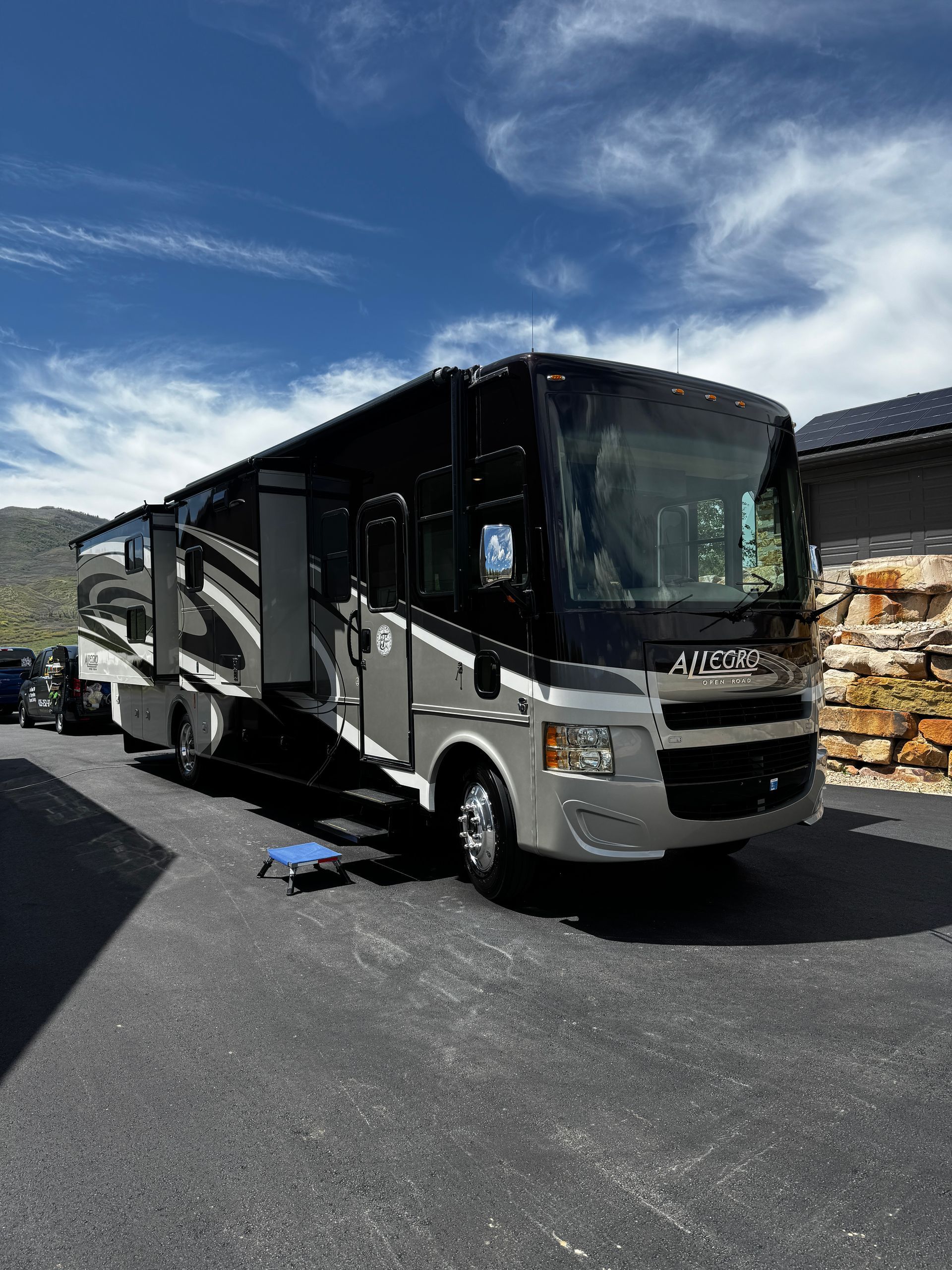 Large black-and-silver RV parked on a paved lot under a blue sky