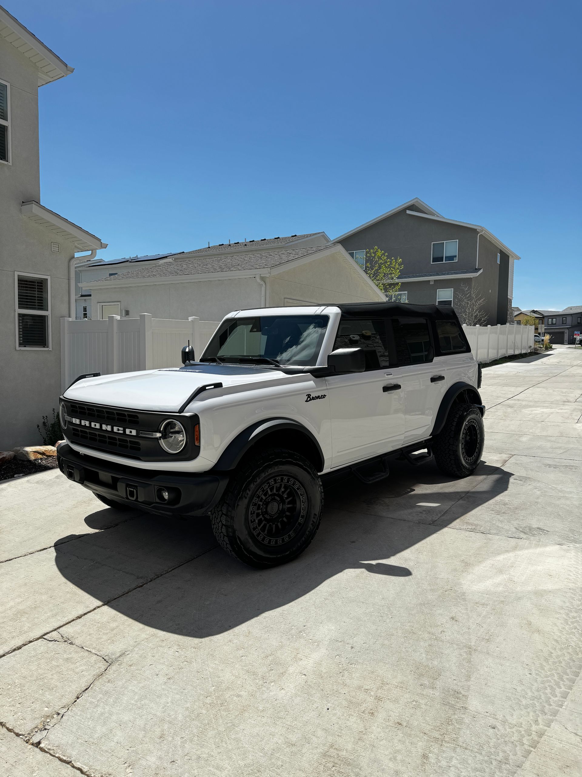 White SUV parked in a sunny residential driveway beside beige houses and a blue sky
