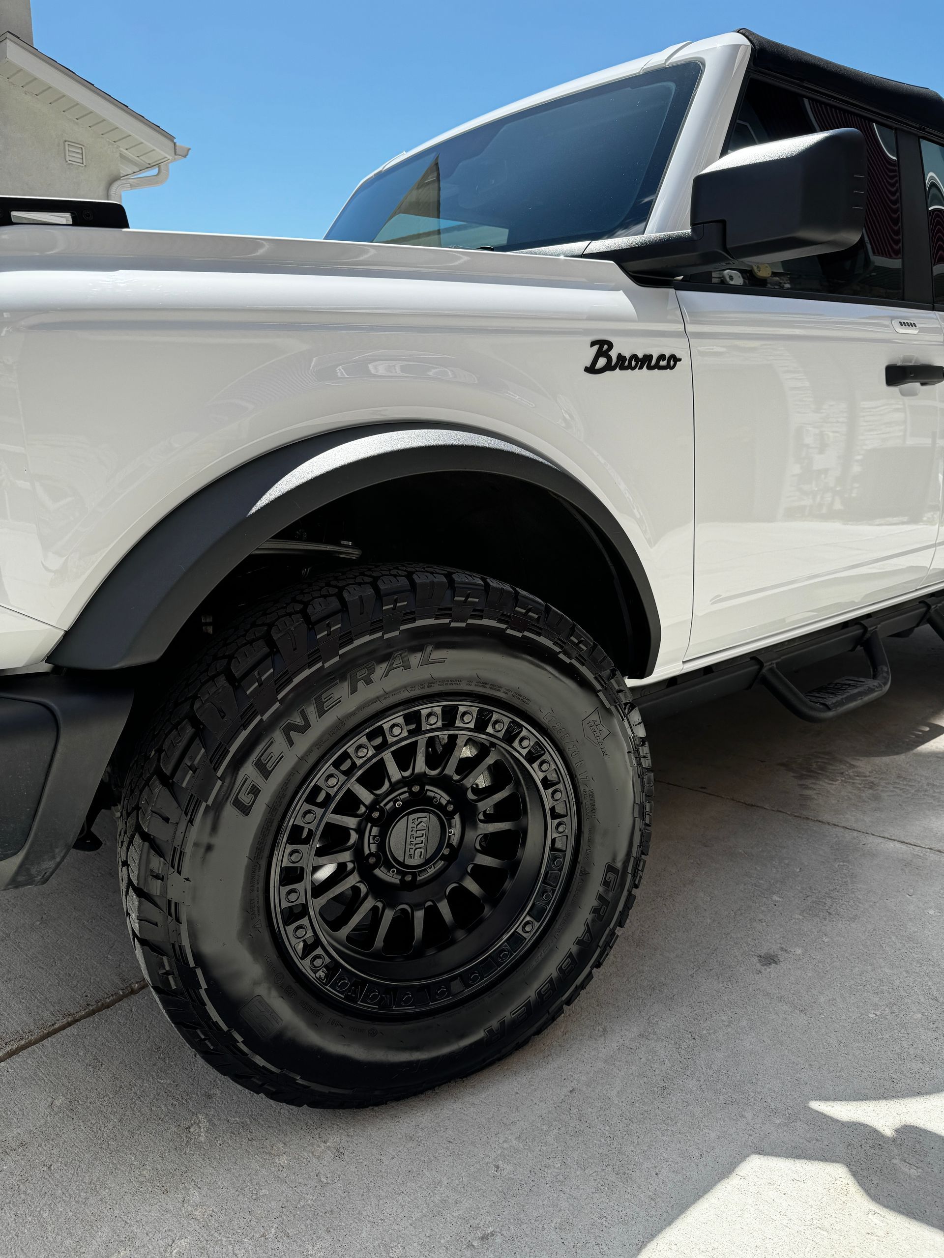 White Ford Bronco with black off-road wheels parked in a sunny driveway